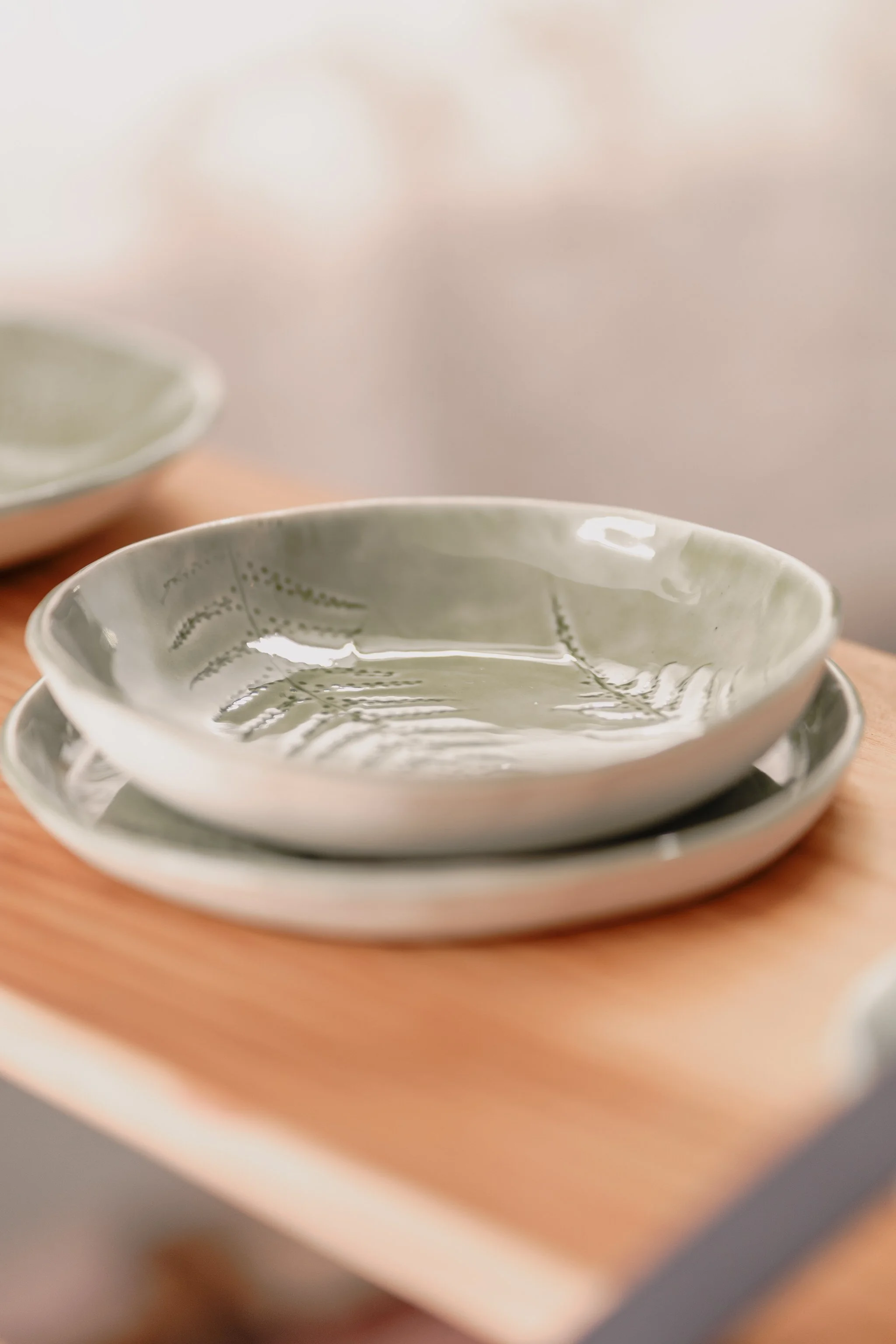 Close-up of green ceramic bowls with textured fern design on a wooden surface.