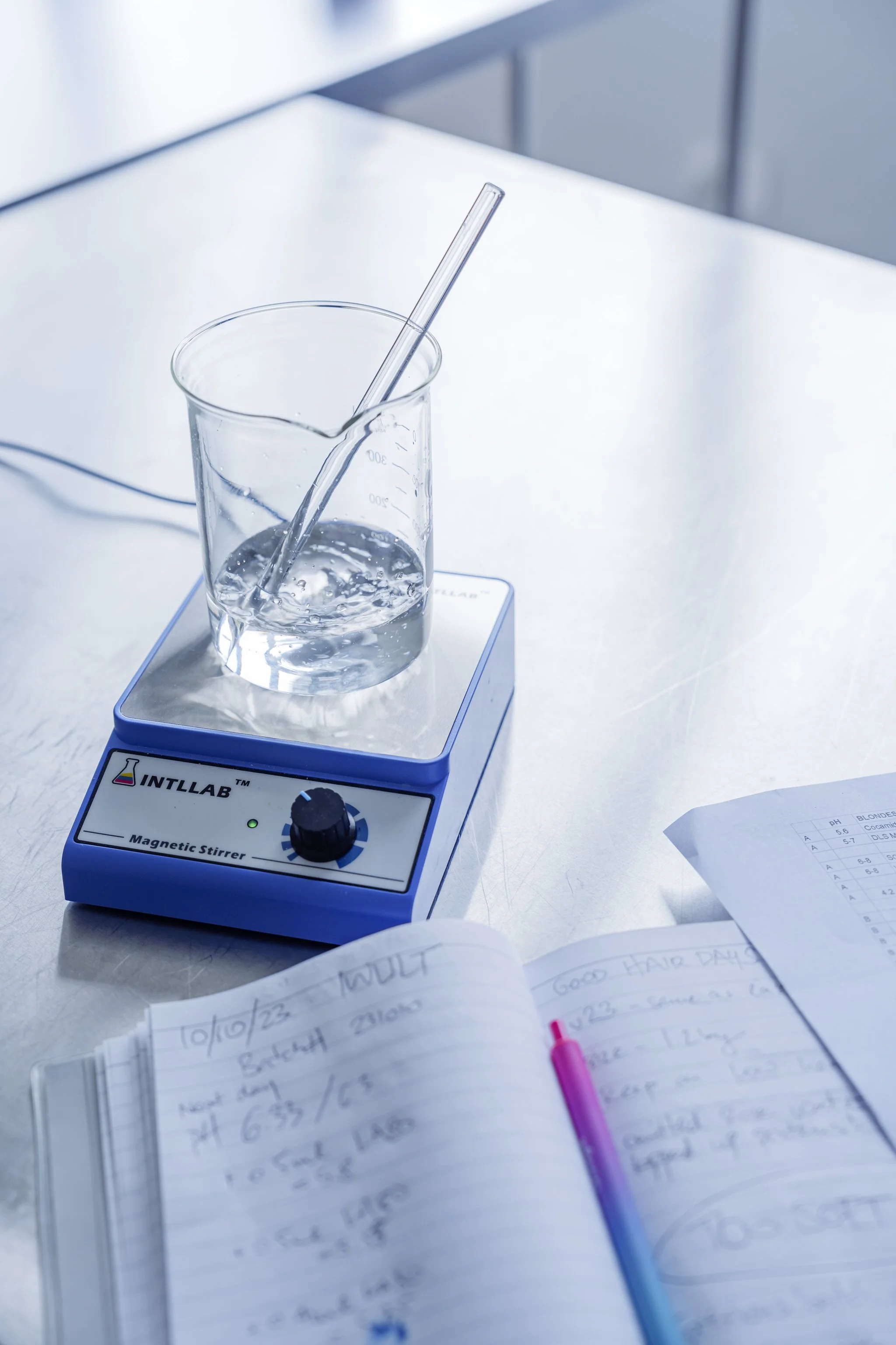 Laboratory setup with a beaker containing liquid on a magnetic stirrer, with notebooks and notes nearby.