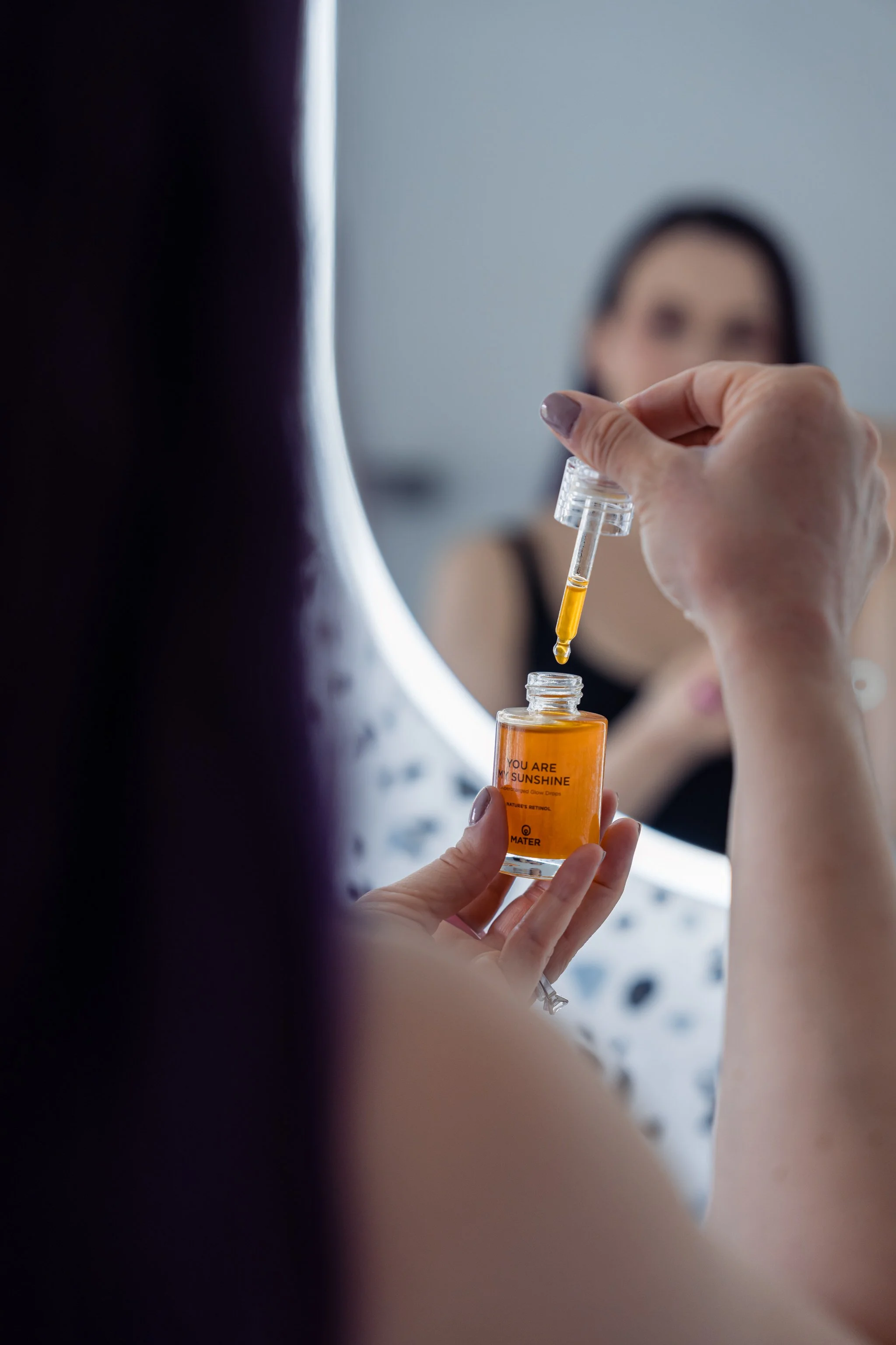 Person holding a dropper and bottle of serum near a mirror