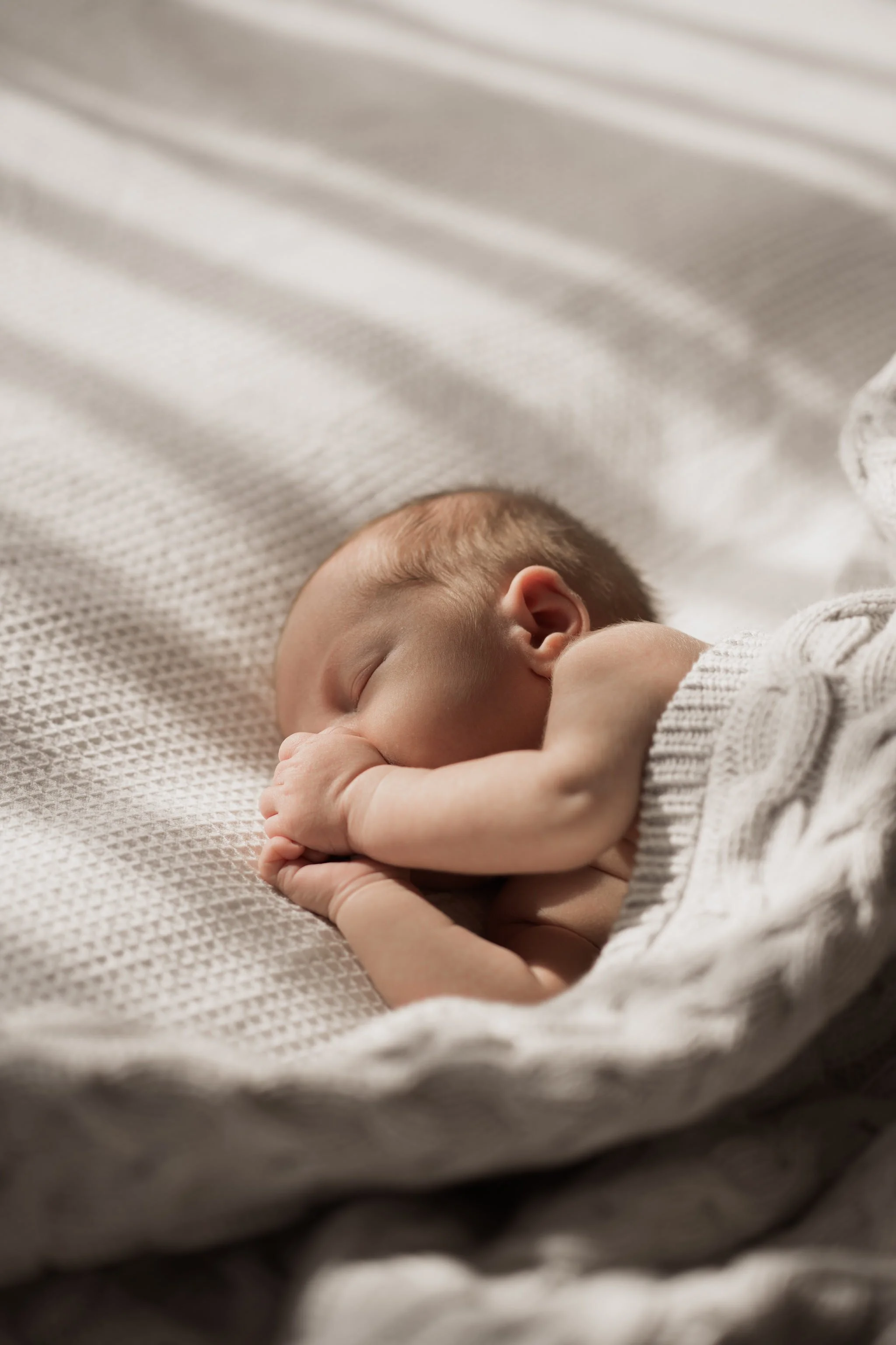 Newborn baby sleeping under a knitted blanket.