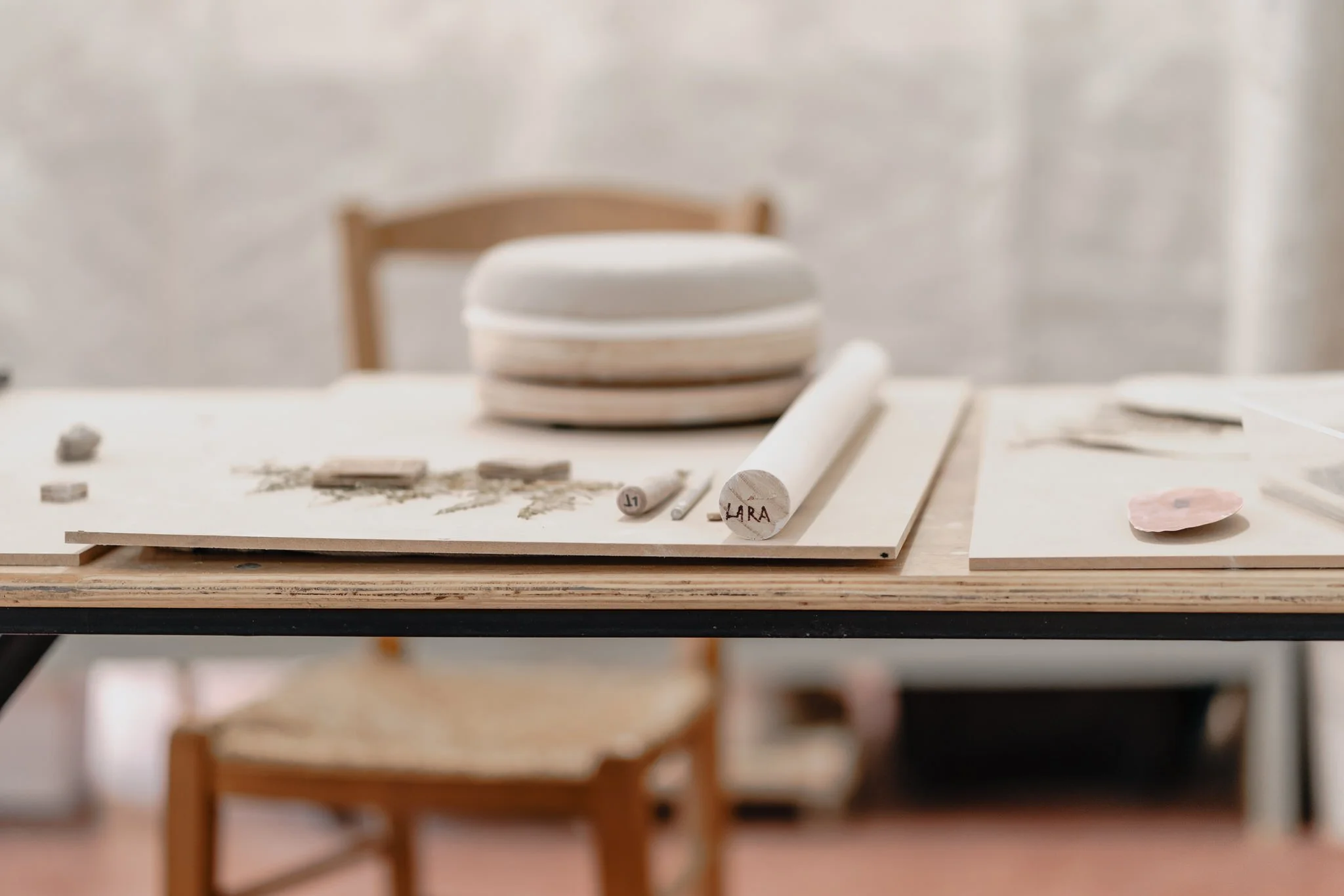 Close-up of a pottery workspace with clay pieces, a rolling pin, and a wooden chair in the background.