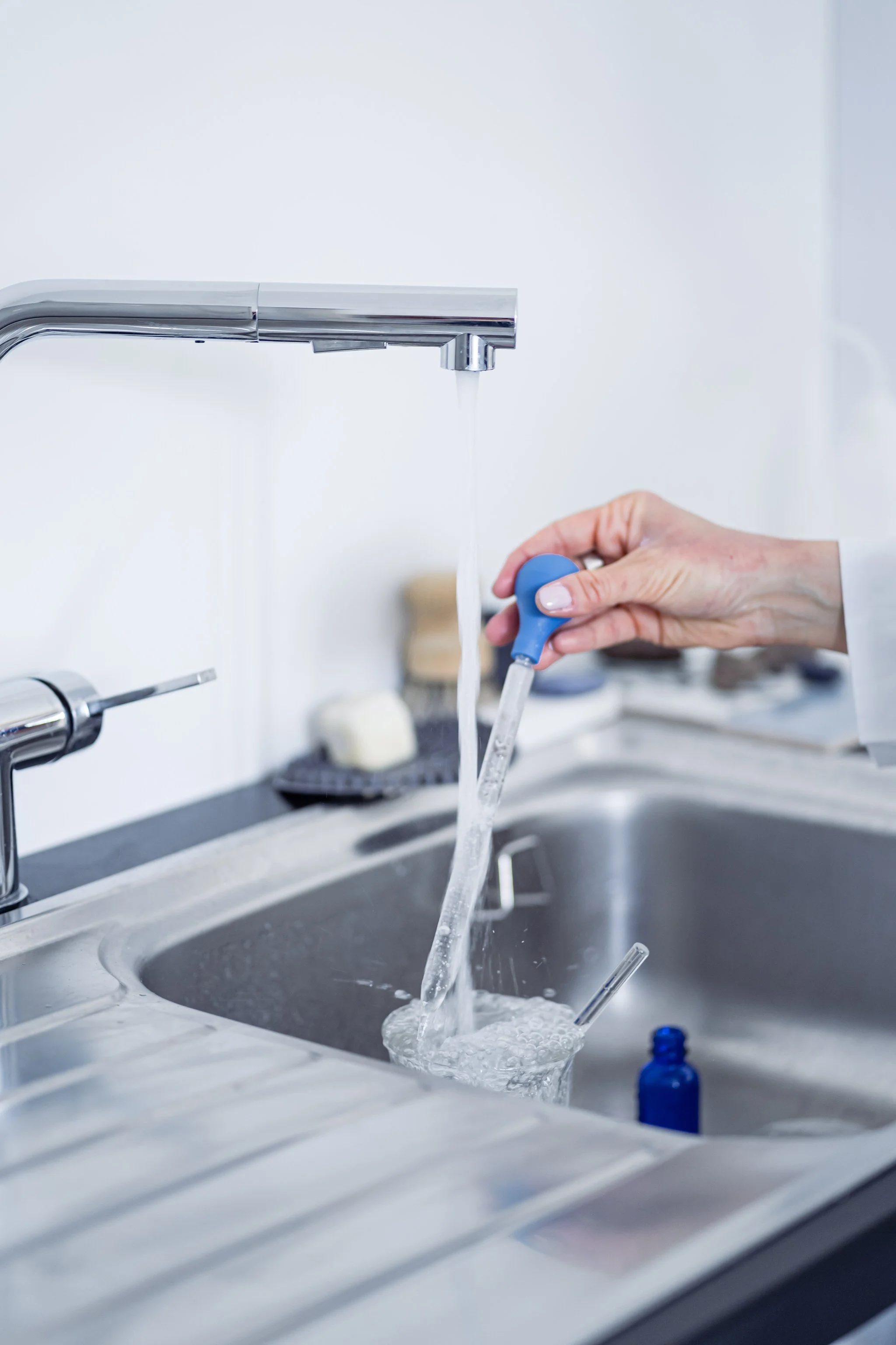 Person filling a glass with water from a kitchen faucet using a pipette.
