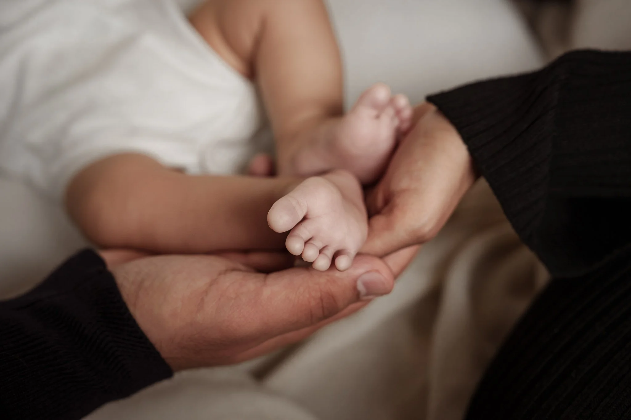 Close-up of a baby's feet held gently by adult hands.