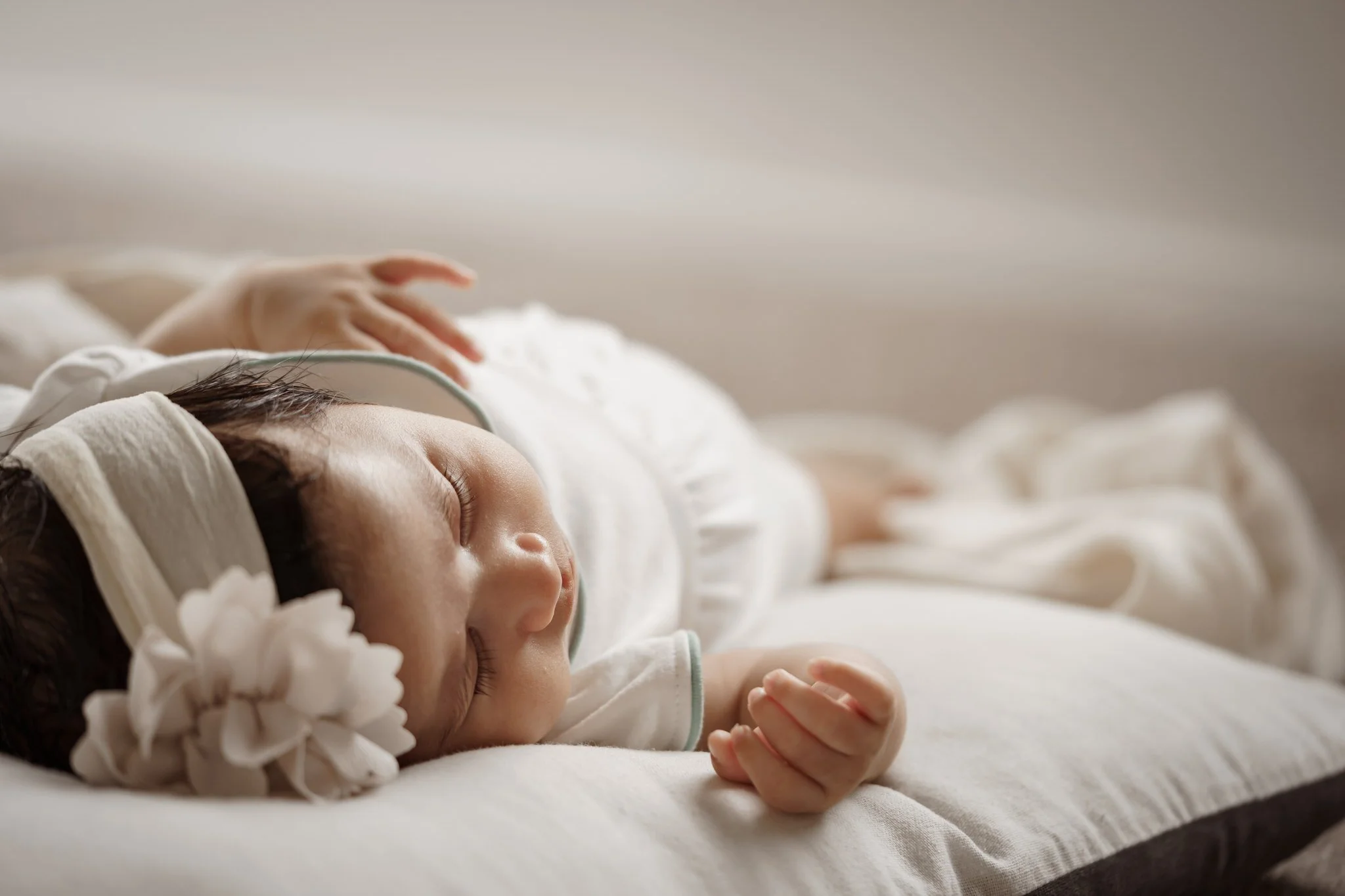 Sleeping baby with headband and flower on a pillow.