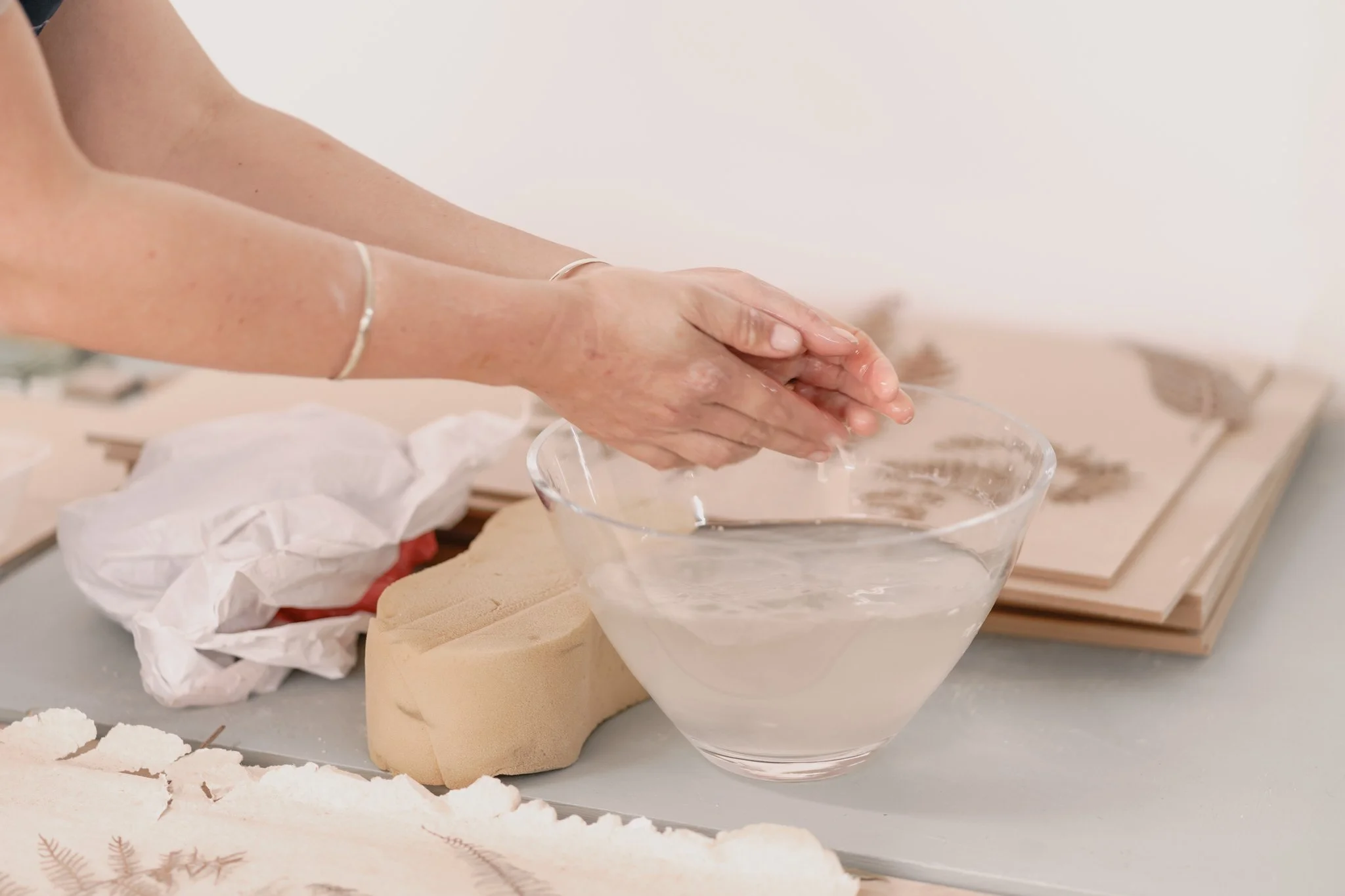 Person crafting with a bowl of water, sponges, and paper with leaf prints.