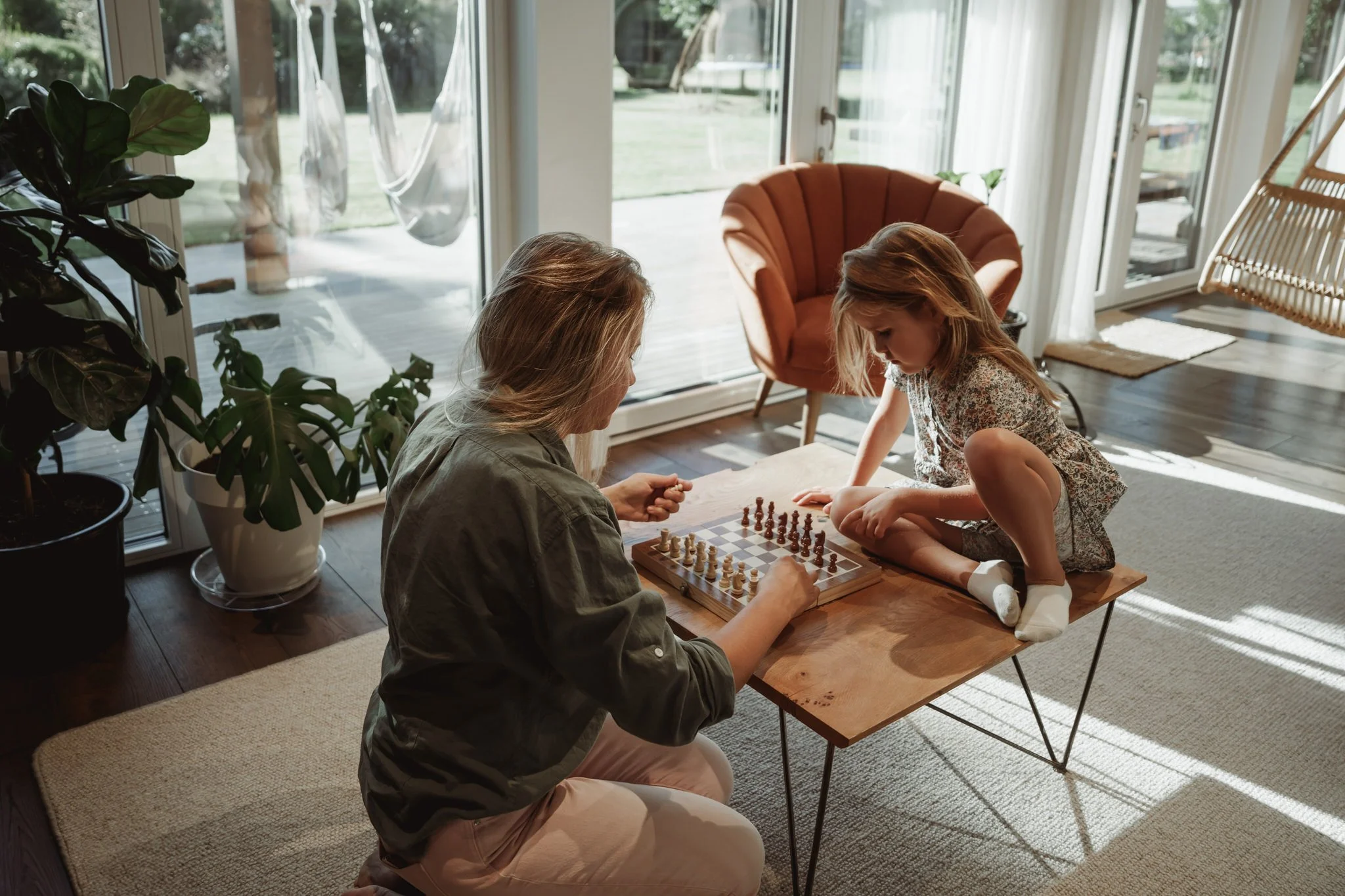 A couple walking barefoot on Muriwai beach near a large rock formation along the shoreline. The sky is overcast and the ocean waves gently reach the shore. The couple is holding hands.