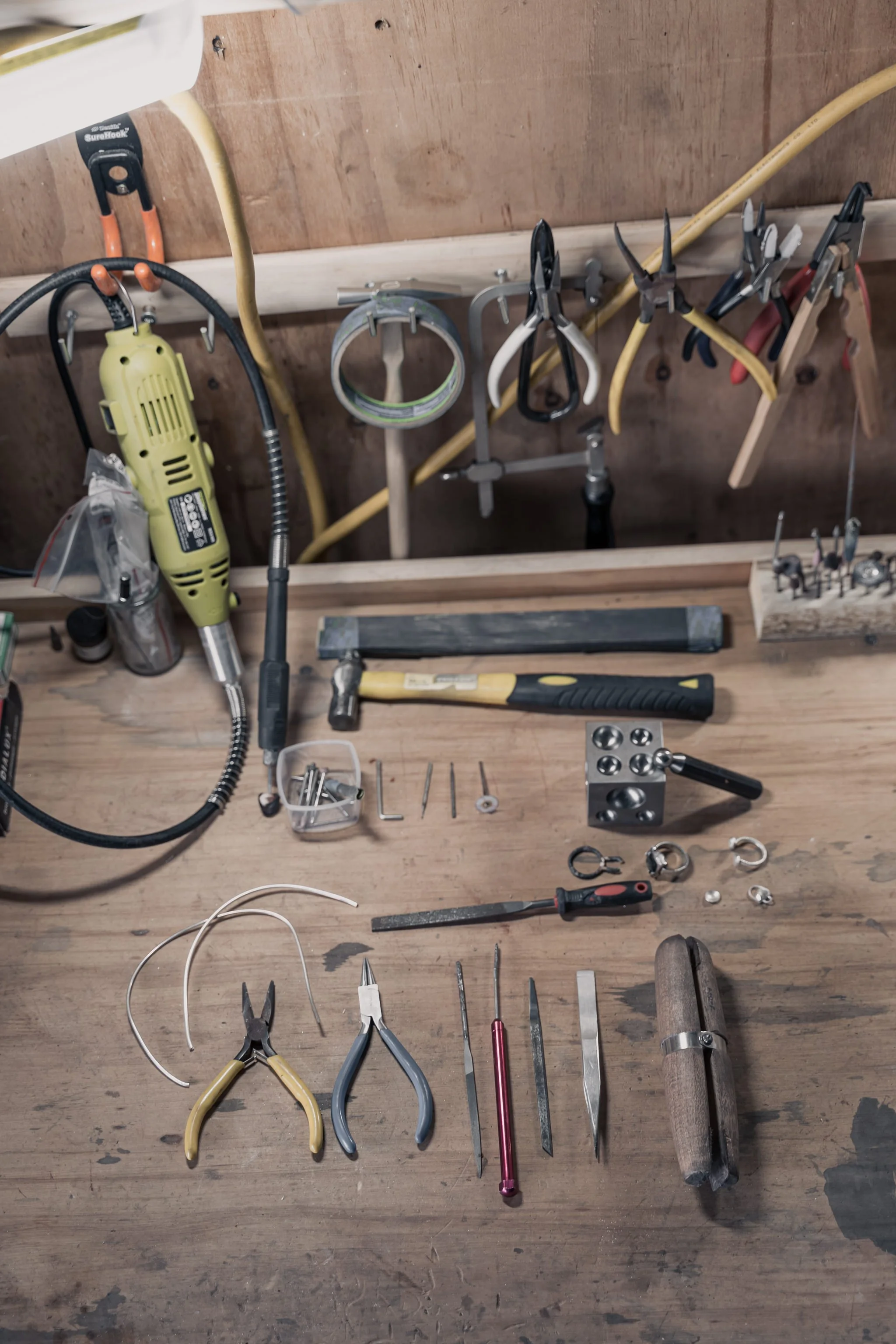 Jeweler's workbench with various tools including pliers, files, a hammer, a drill, and precision instruments.