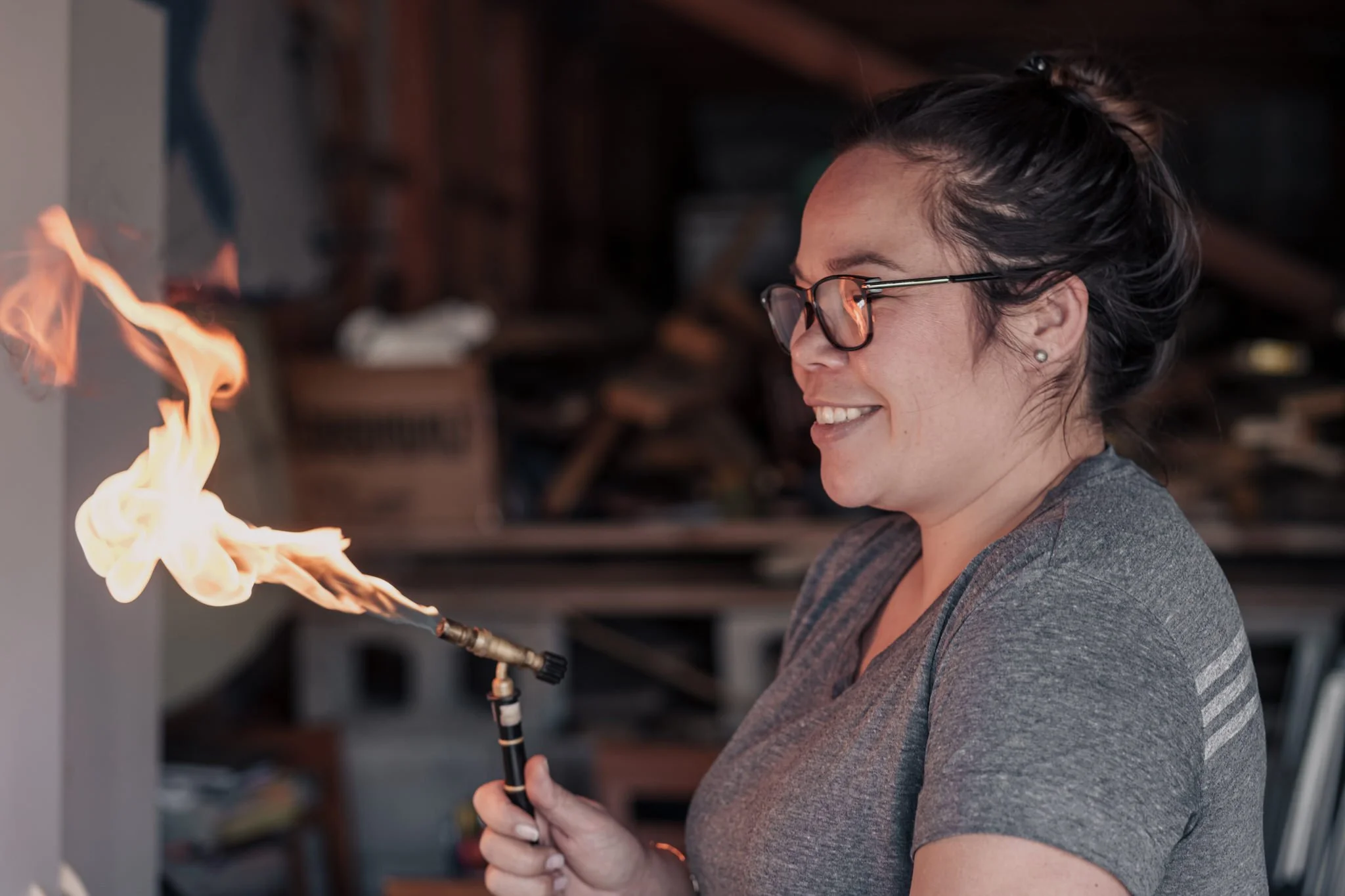 Person using a blowtorch with flames, wearing glasses and a gray shirt.