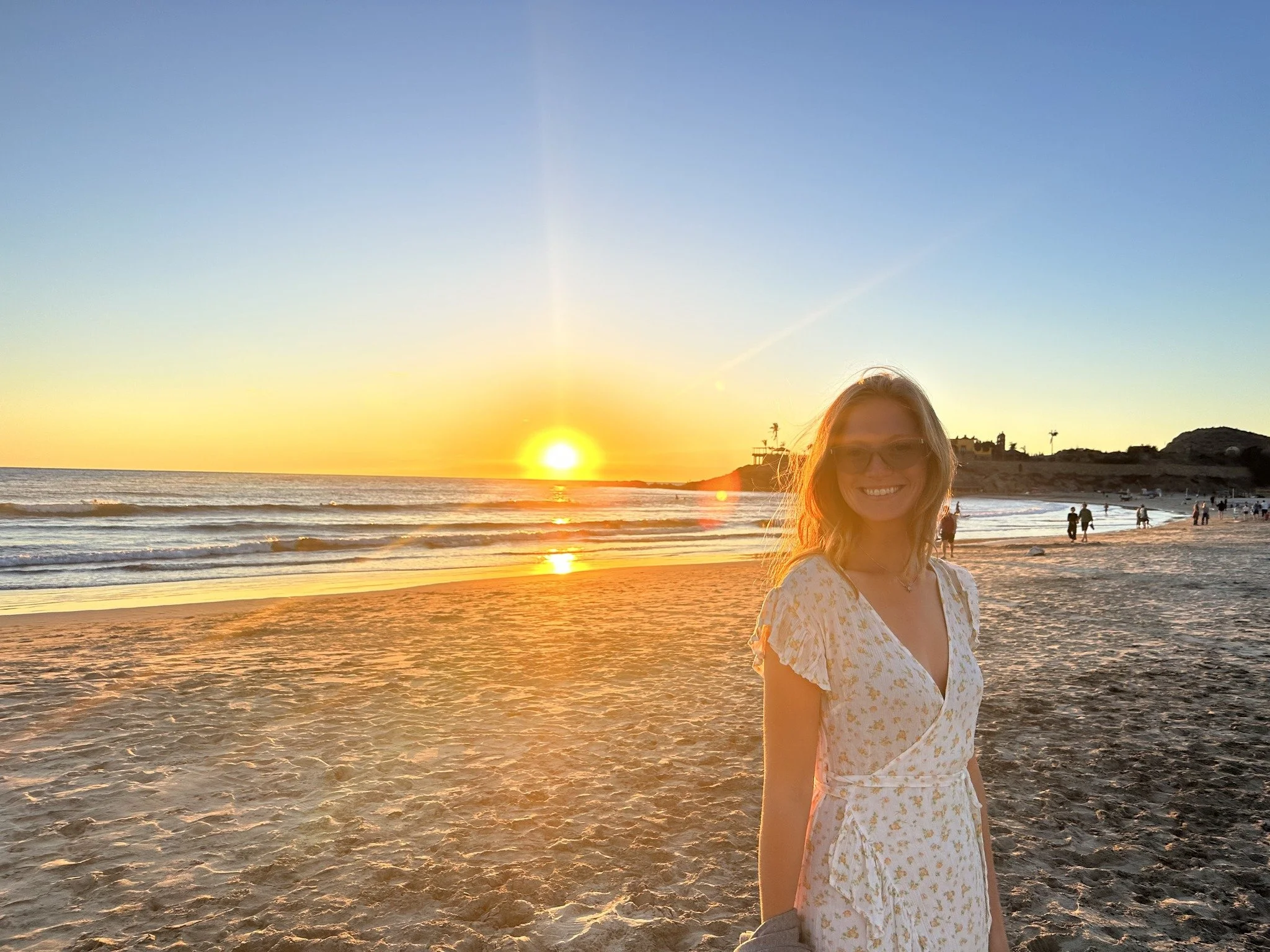 woman standing on the beach smiling with the sunset