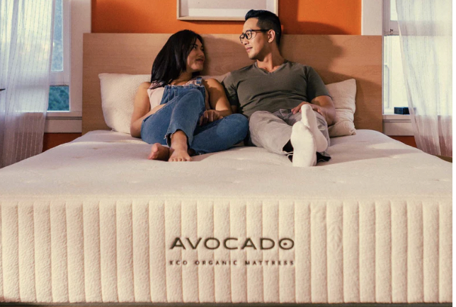 two people sitting happily on a new Avocado brand mattress