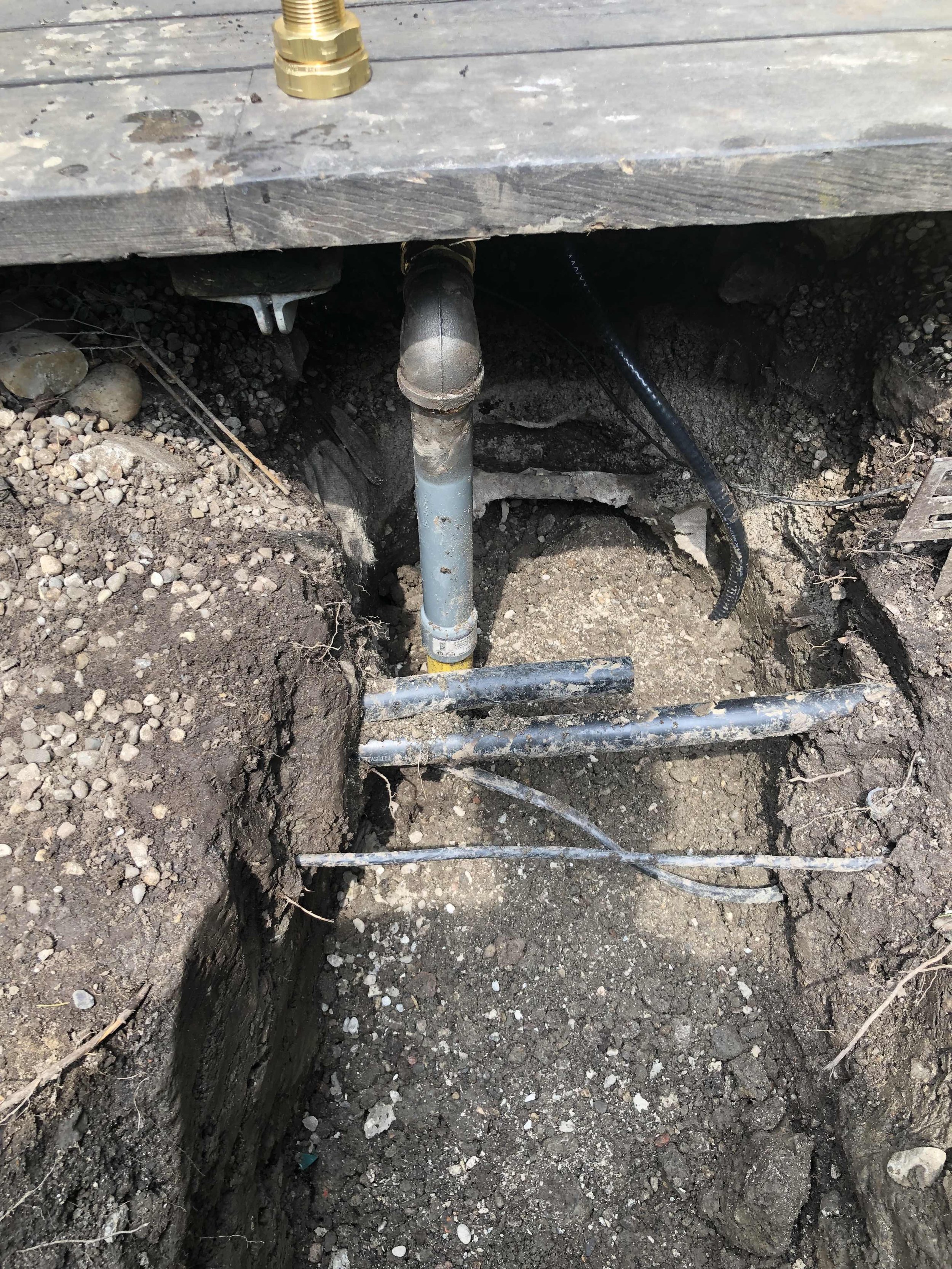 A plumbing pipe installation in a trench at a construction site with dirt and rocks surrounding it.