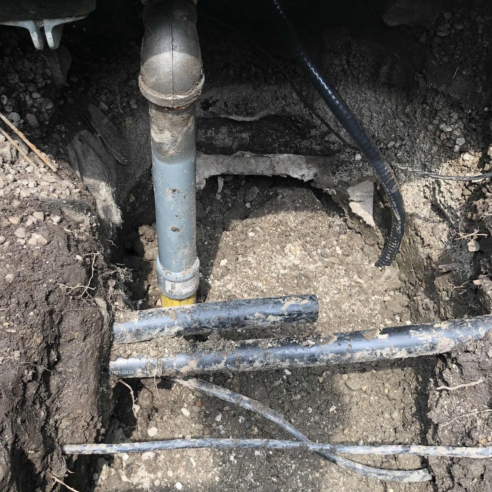 Underground utility pipes and cables installed in a trench with excavated soil and rocks.
