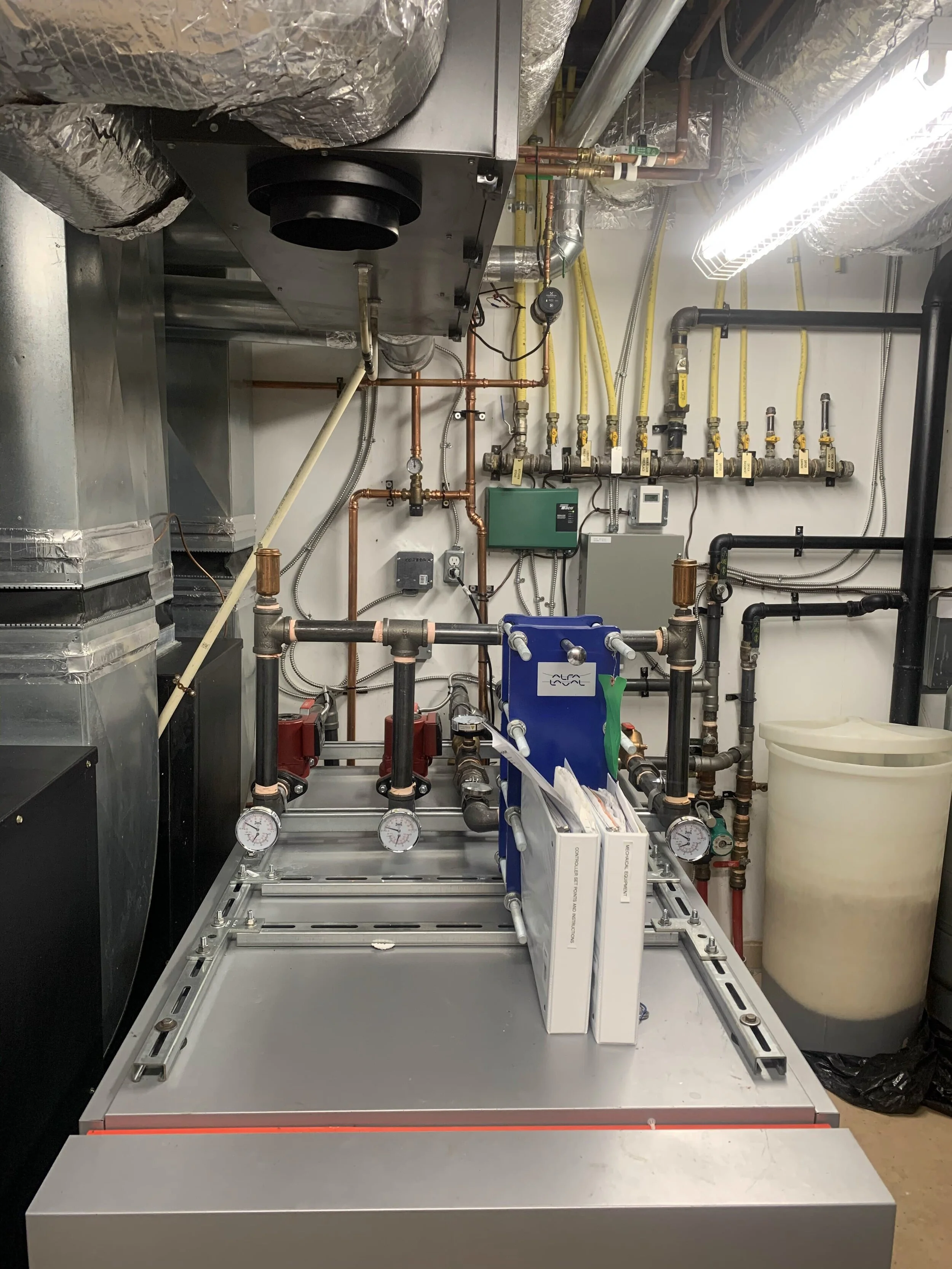 Industrial mechanical room with pipes, gauges, and equipment, with a large metal platform and various valves and meters.