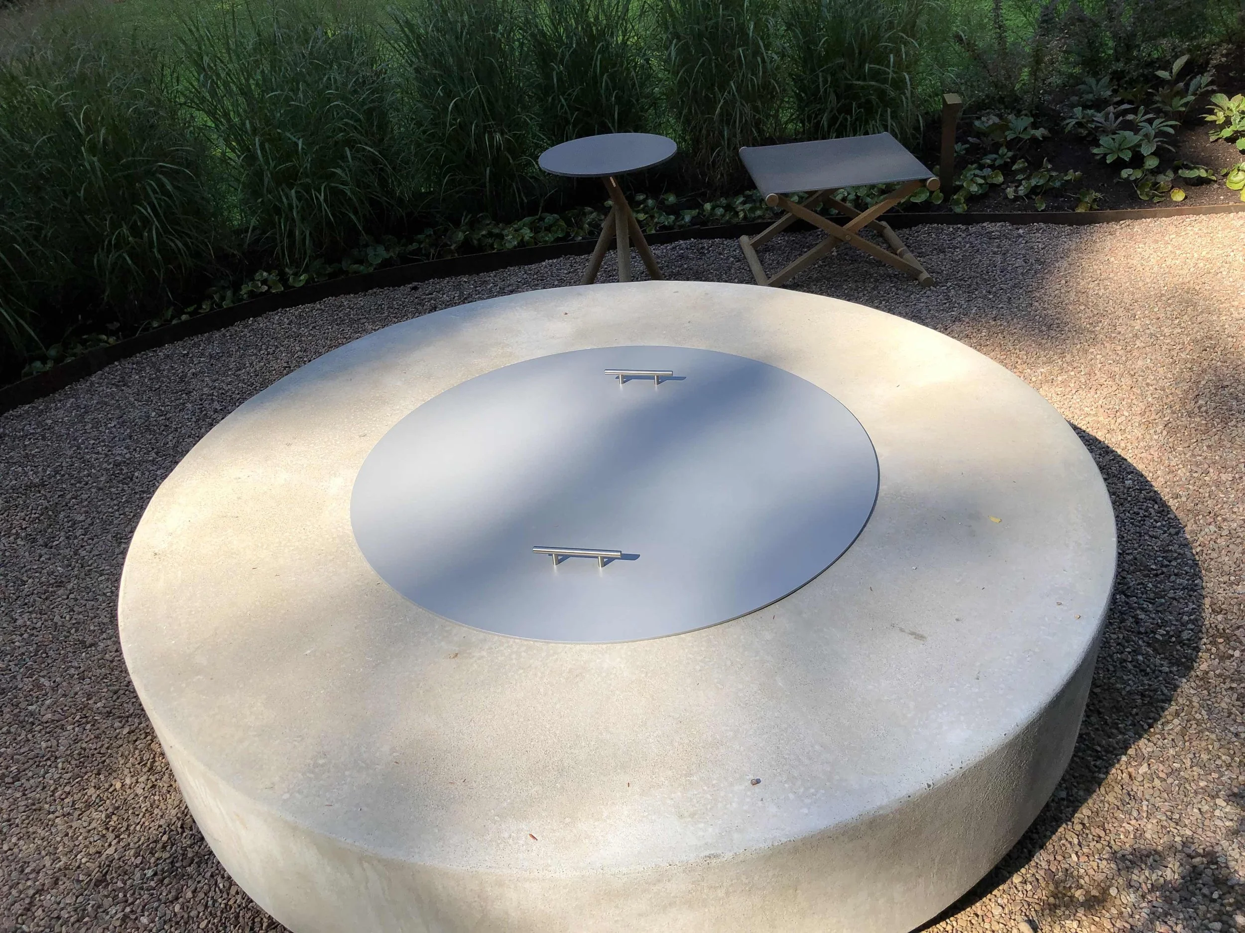 Closed outdoor fire pit, surrounded by green grass and plants.