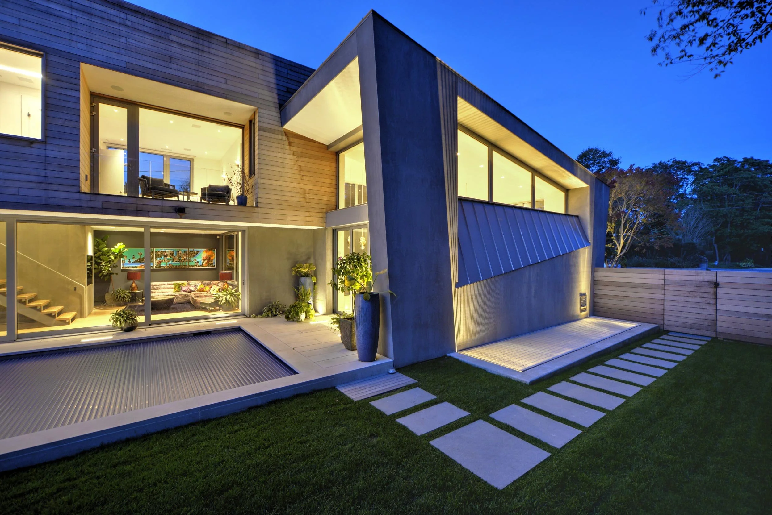 Lane House exterior with cedar siding rainscreen, smooth stucco, and standing seam metal roof at night, East Hampton