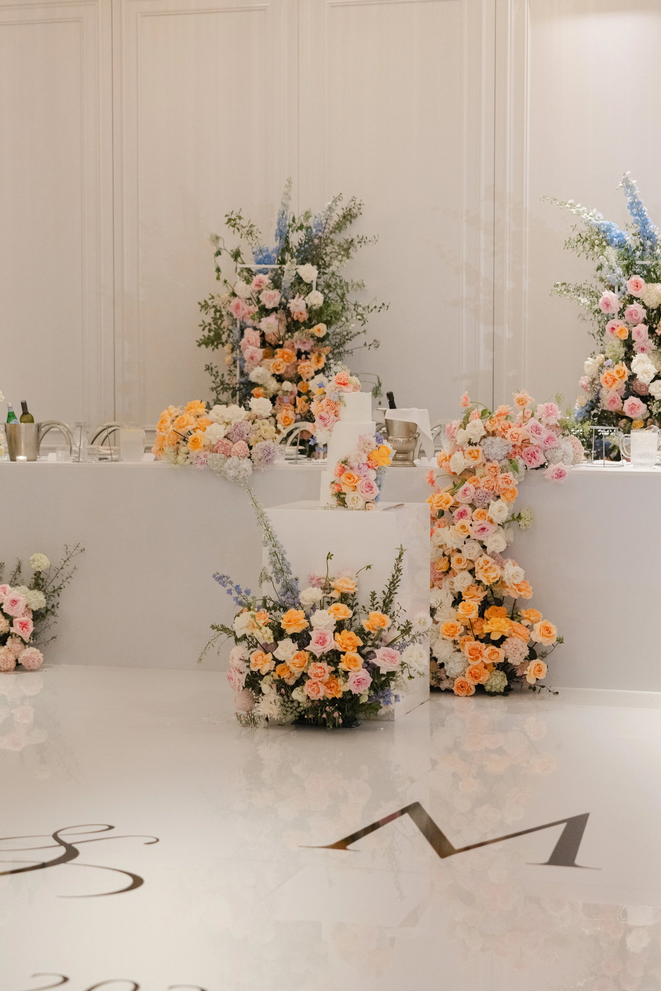 A floral centerpiece with blush roses, white flowers, and greenery on a table set for a formal occasion.