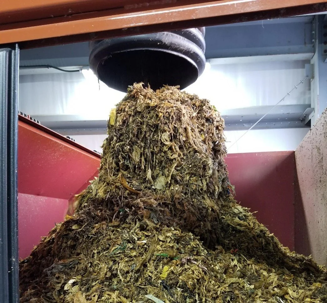 pile of shredded plastics in a red metal bin, coming out of a black tube from above, industrial setting