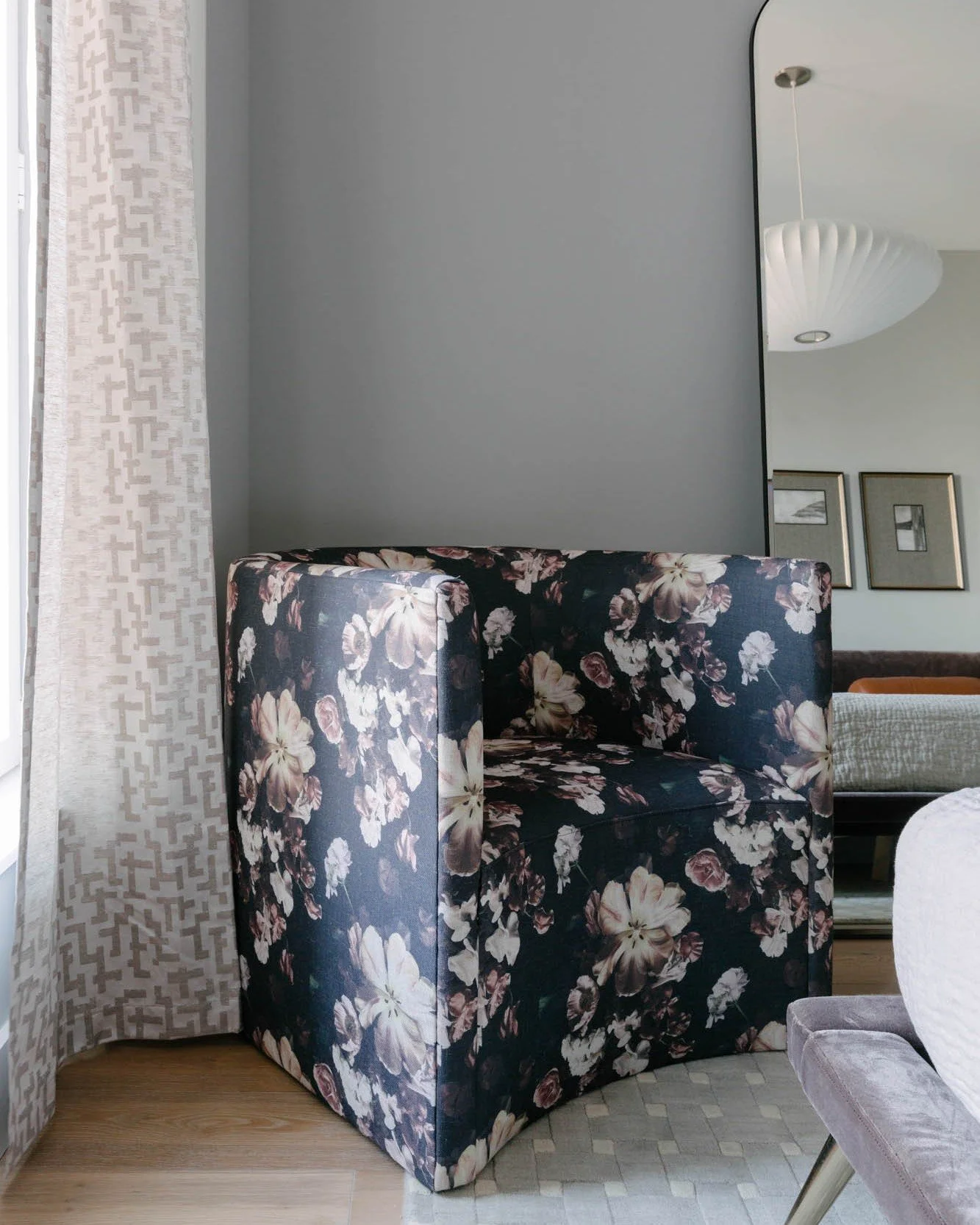 Layers do the work in this room.

We built depth through texture&mdash;a woven trellis rug, silk taffeta curtains, and a quilted coverlet &mdash;all in the same tonal palette but never flat. Then we brought in a moody floral chair and a chocolate vel