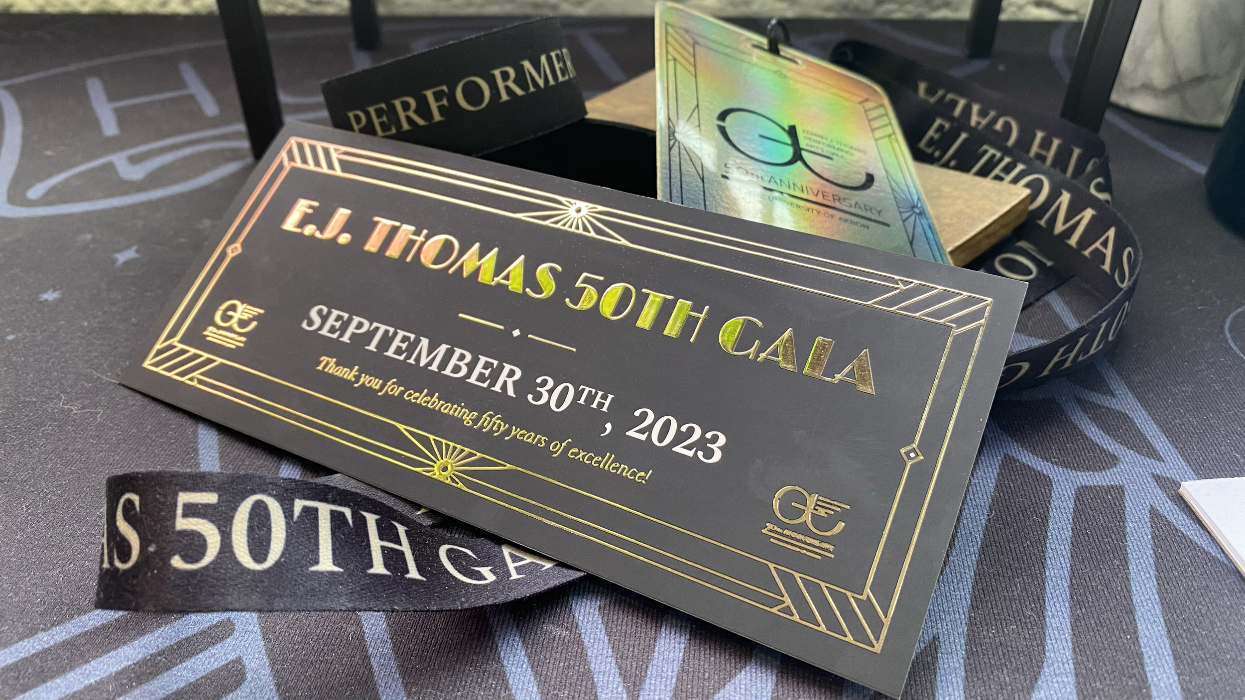 A collection of elegant, custom-designed event credentials (including golden tickets, laminate passes, branded lanyards, and event wristbands) for a 50th anniversary donor engagement event on Division 1 university campus.