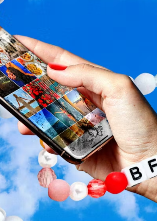 Close-up of a person's hand holding a smartphone with a collage of colorful images on the screen, against a blue sky background.