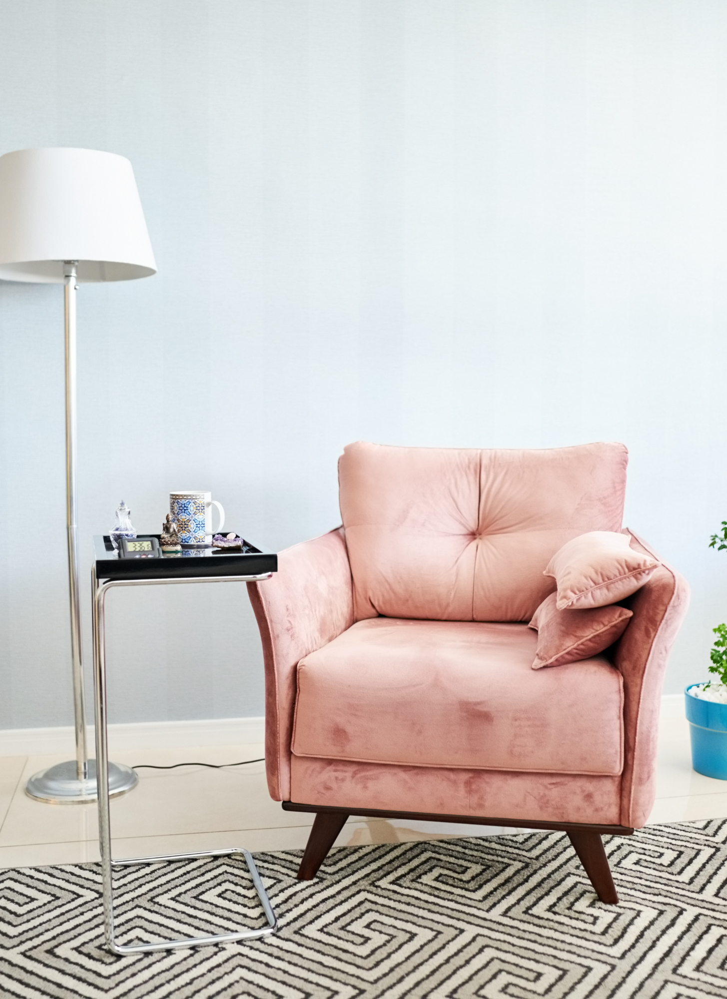 Cozy living room with pink armchair, floor lamp, side table with mug and knick-knacks, on patterned rug.