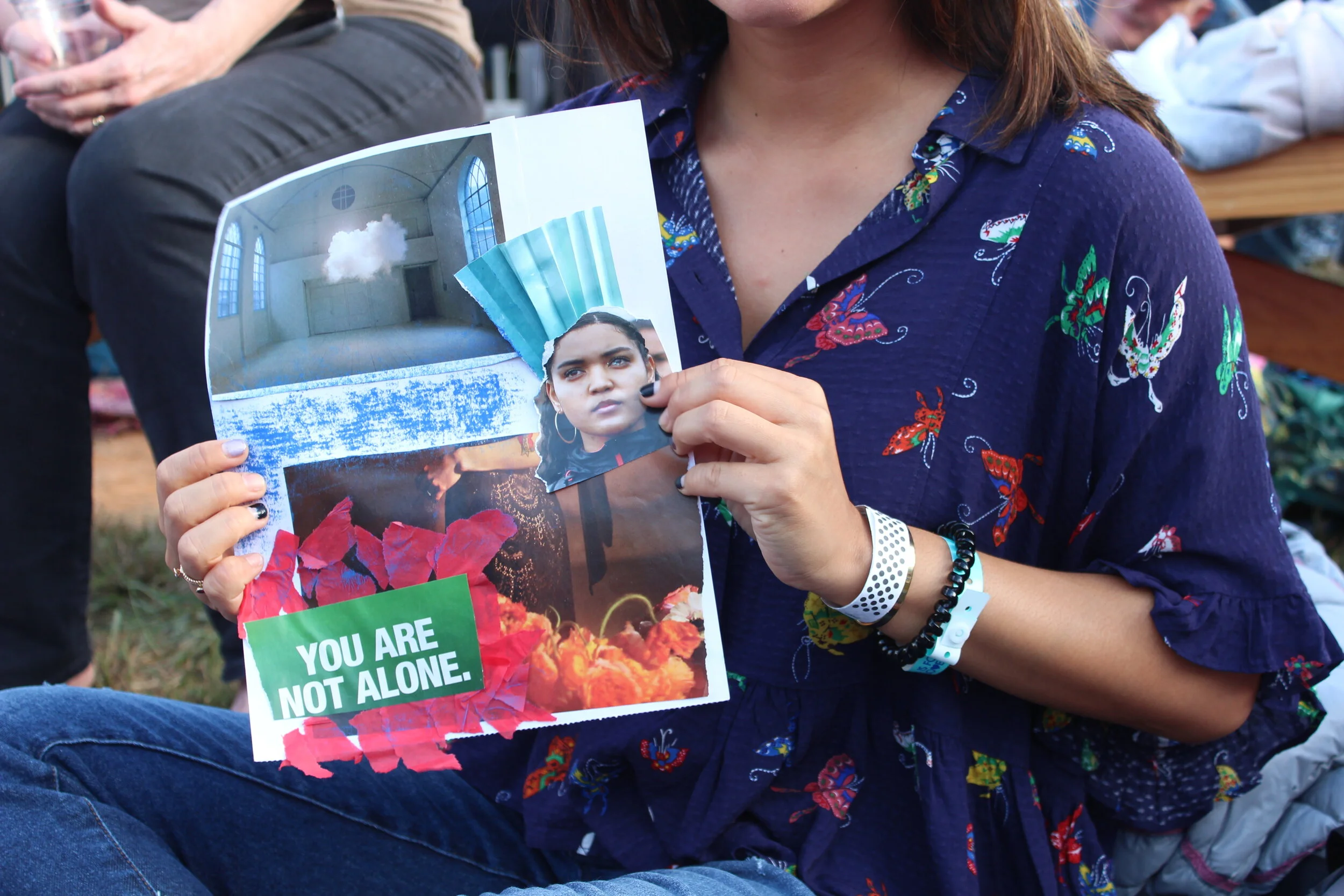 Art Therapist, Emily Davenpor, leading a wellbeing workshop for a Workplace Wellness Event featuring a woman with brown hair wearing a blue floral shirt holding a flyer with a picture of an indoor space and a young girl's face