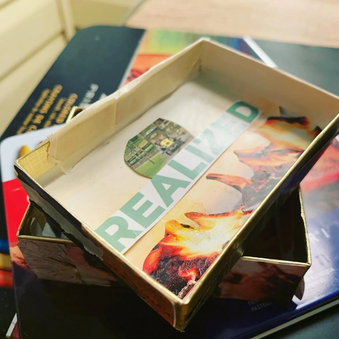 A board game box with a fiery landscape on the cover, and a partially visible game piece or card inside. The box has a sticker with an aerial view of a city or landscape, and the word 'PEACE' partially visible.
