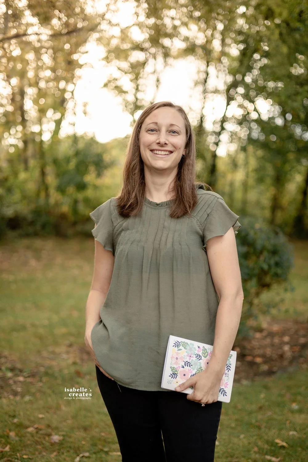 Woman standing holding her floral notebook with trees and sunset behind her in Indiana.