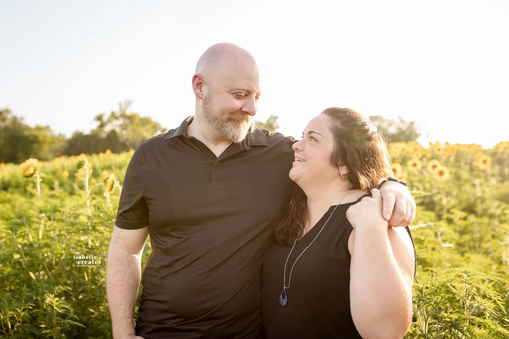 Leslie and Gabriel smiling among tall sunflowers at sunset during their Missouri engagement session.