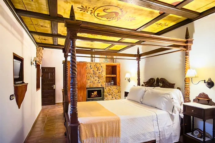 Habitación Superior Deluxe Rústica en La Casa del Rector, hotel con encanto en Almagro; estancia de 36 m² con cama con dosel, salón con chimenea, zona de lectura con vistas al estanque y bañera de piedra para dos personas.