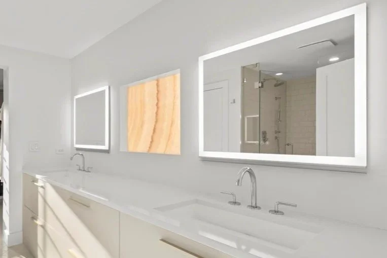 Modern bathroom with a white countertop, two sinks, large illuminated mirrors, and a shower visible through the reflection of the mirror.