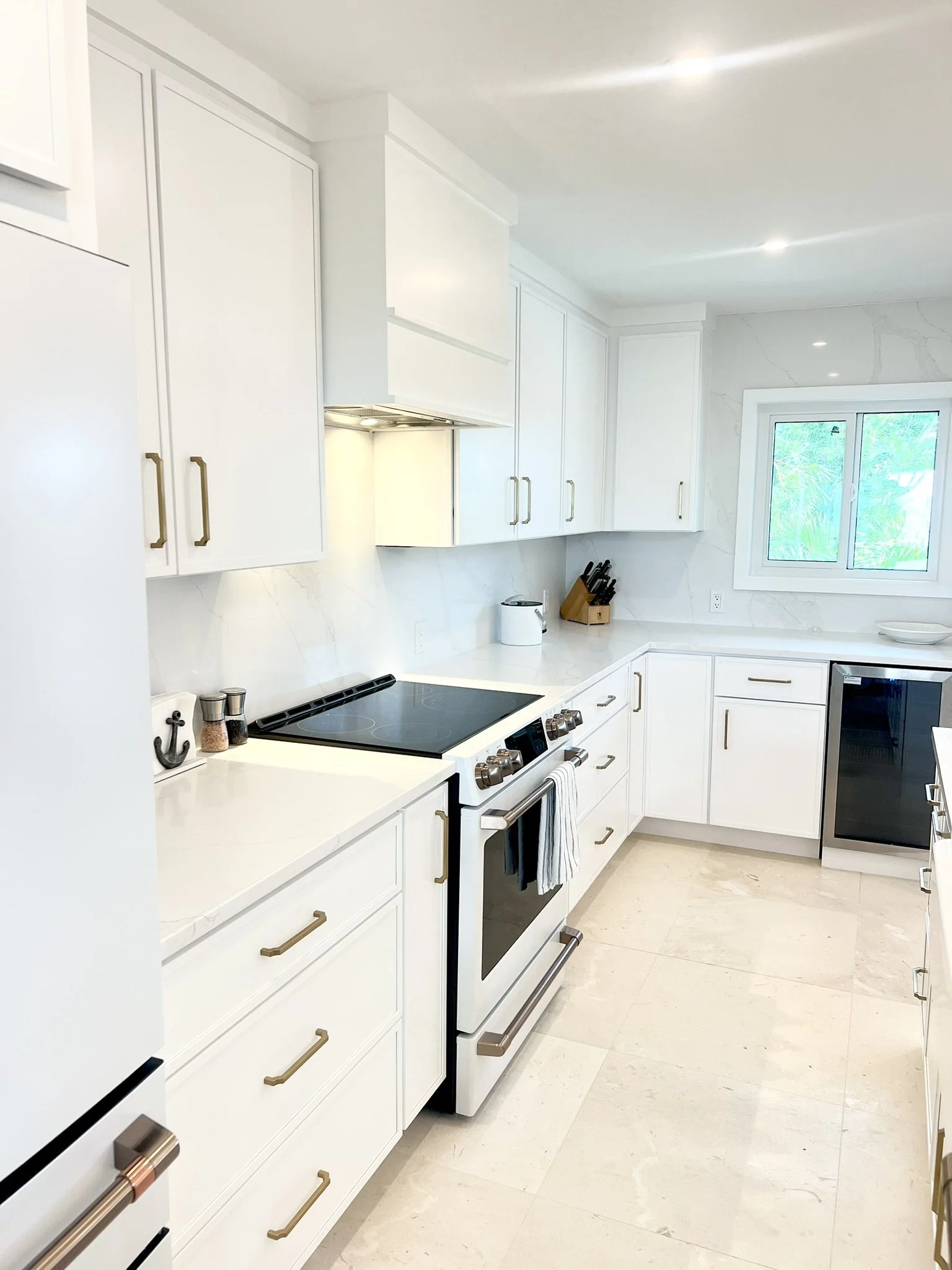 Modern white kitchen with gold handle cabinets, black and white stove, small window, and countertops with kitchen utensils.