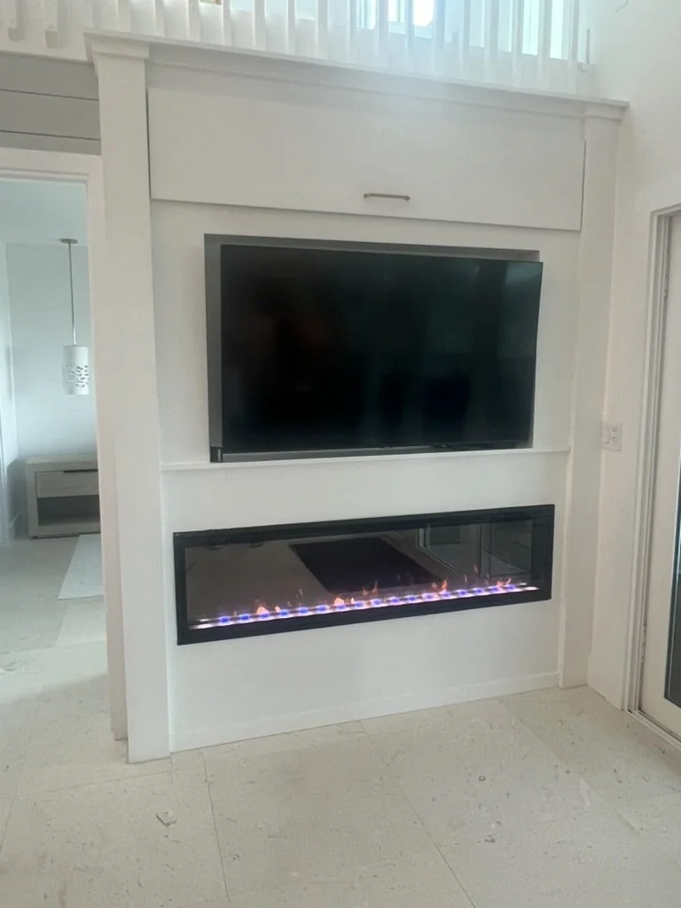 Living room with a wall-mounted flat-screen TV above a modern fireplace with visible flames.