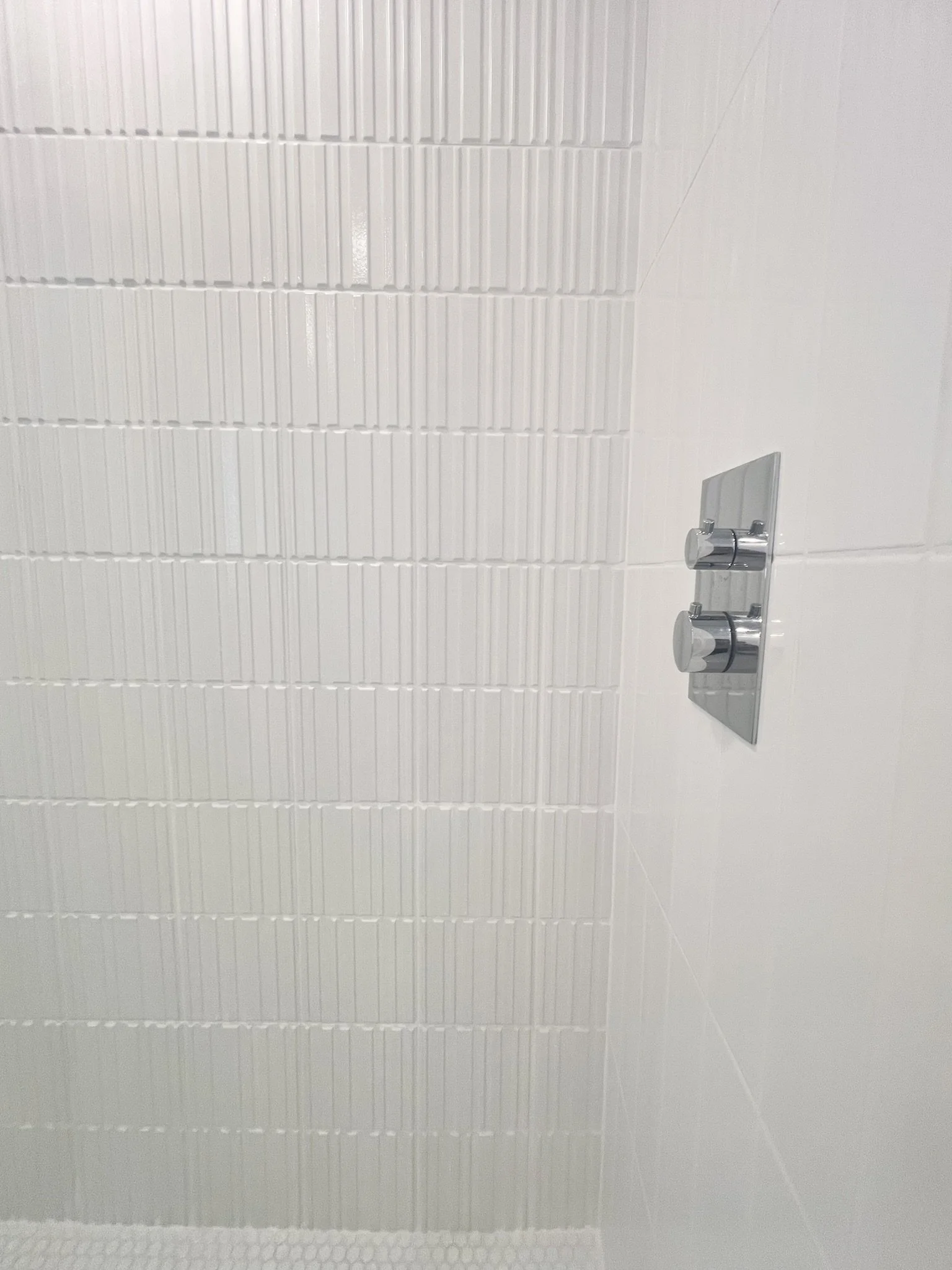 Close-up view of a modern shower with white textured wall tiles and a chrome dual control shower valve.