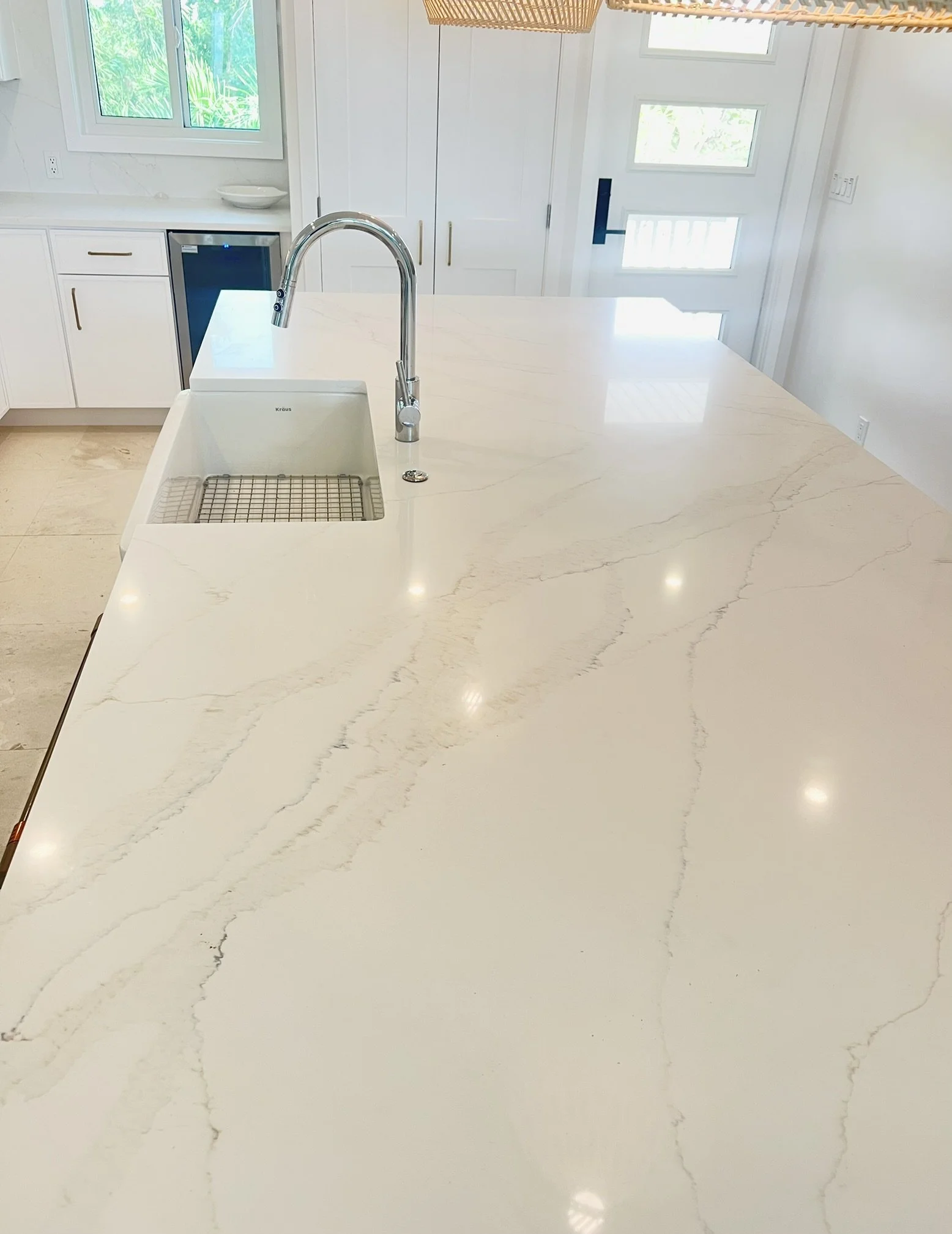 White kitchen island countertop with a built-in sink and a modern faucet, situated in a bright kitchen space with white cabinets and windows.