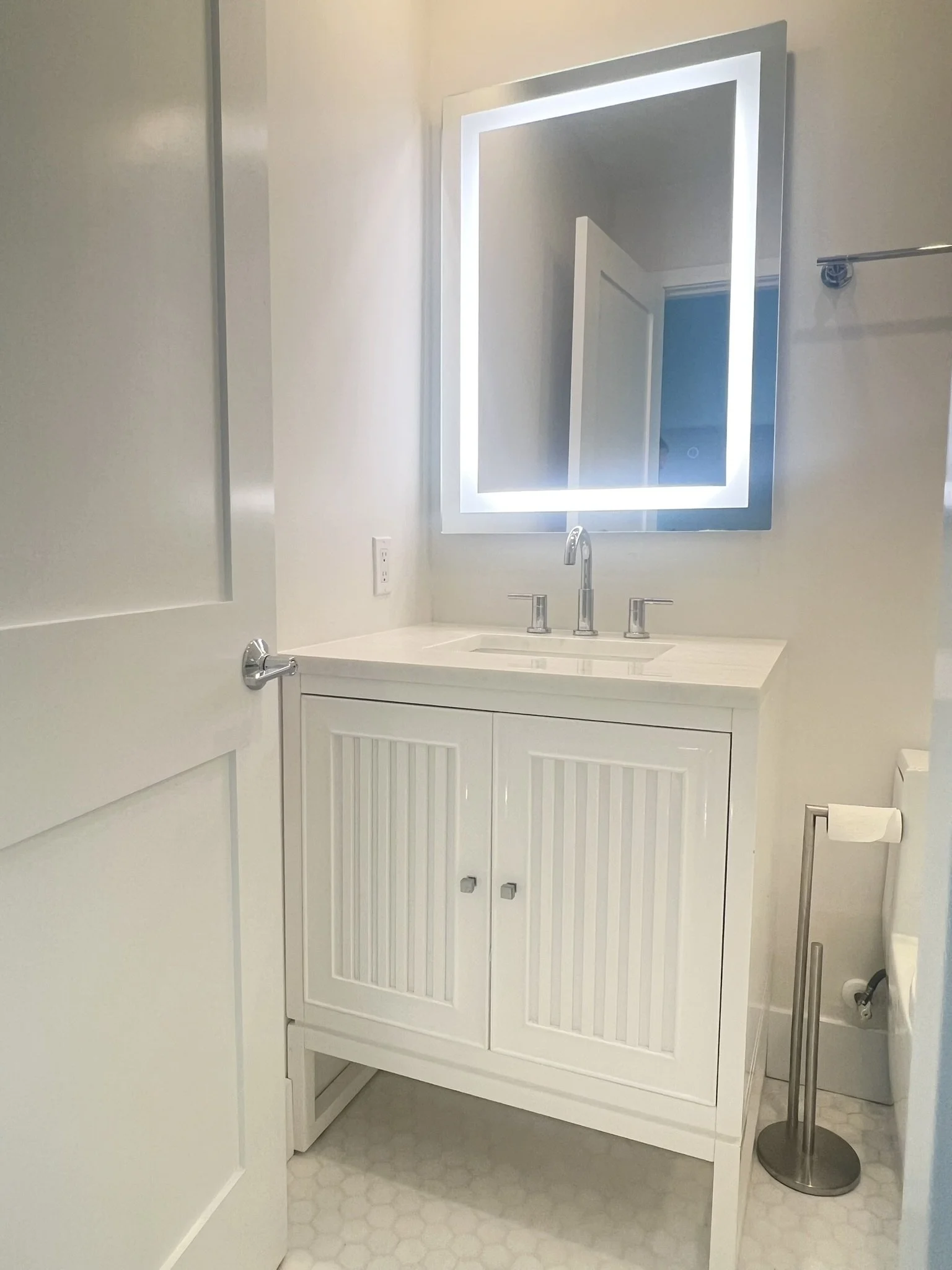 Bathroom with white vanity, illuminated mirror, and a toilet paper holder.