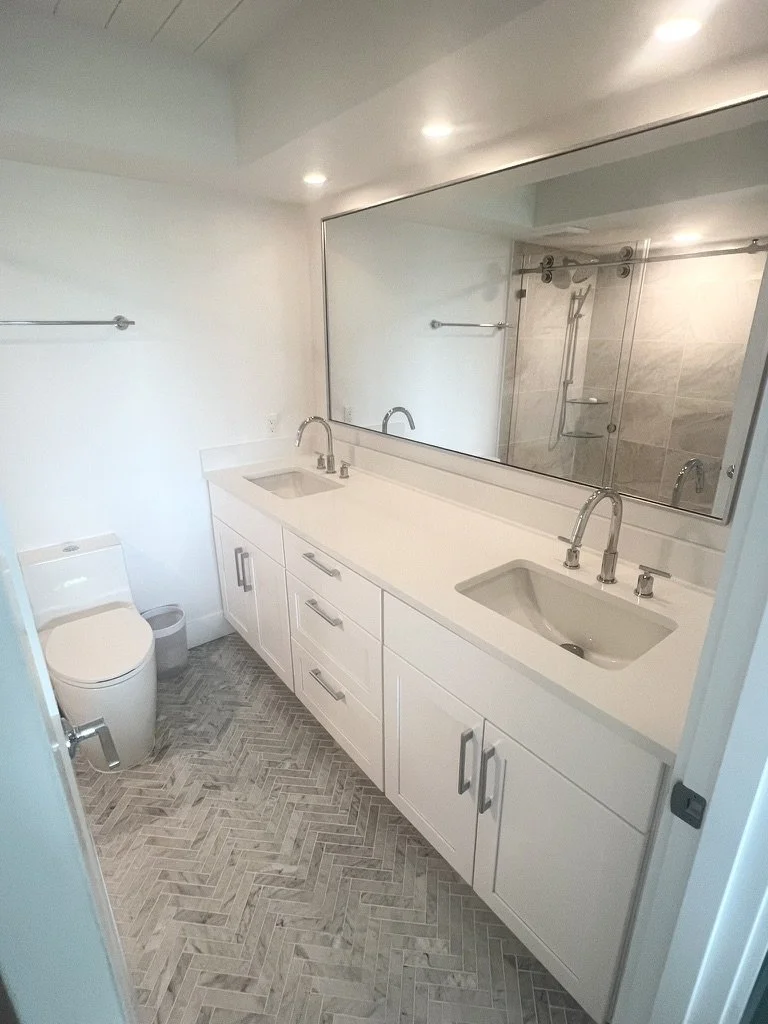 Bathroom with a double vanity with two sinks and large mirror, a toilet, a shower with a glass door, and light-colored tile flooring.