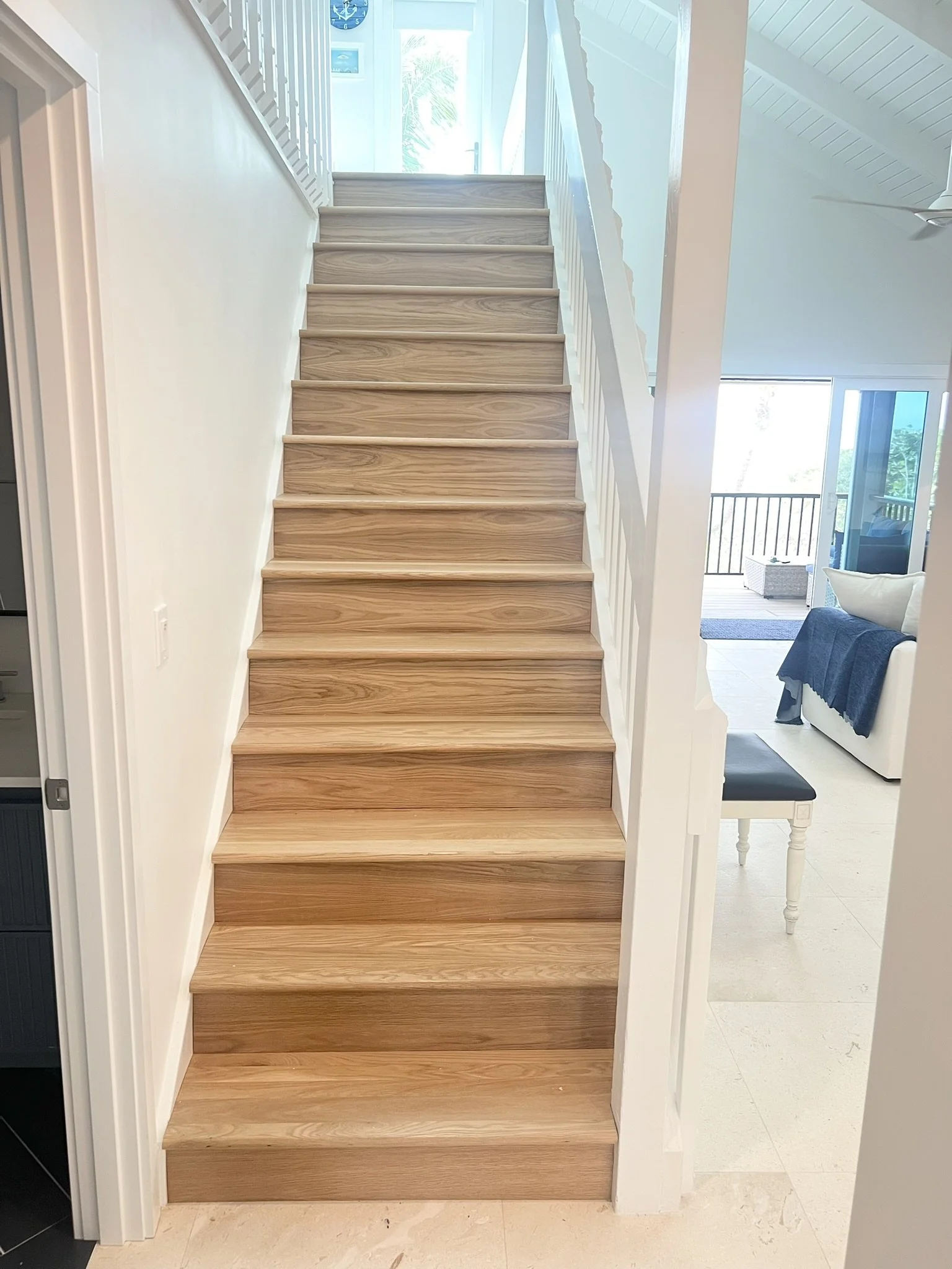 Wooden staircase with white risers leading up to a bright upper floor, with natural light coming through a glass door and windows at the top.