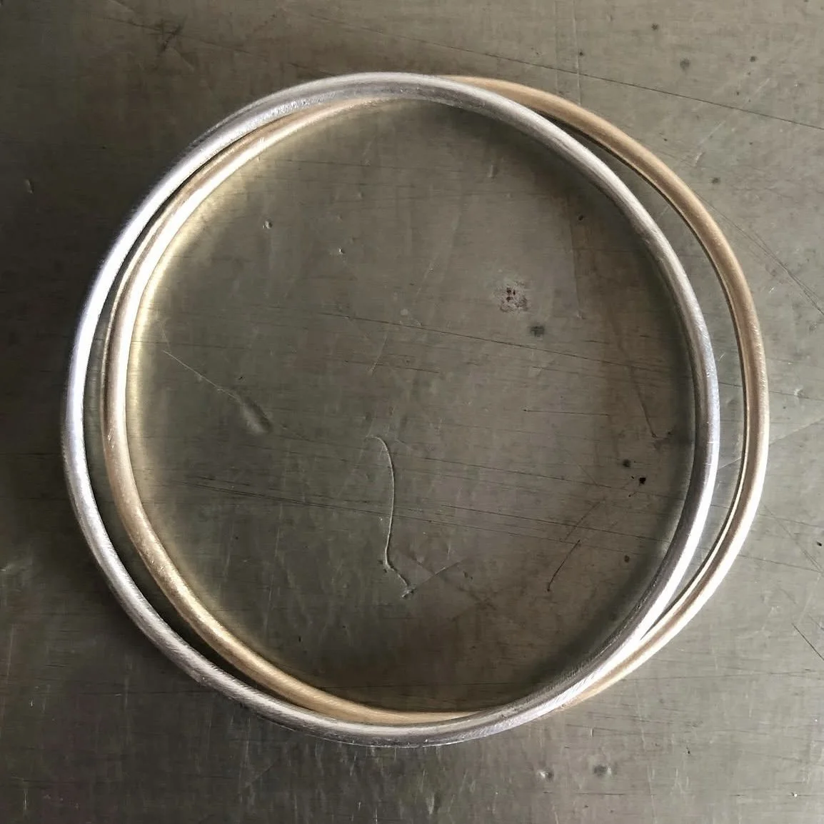 Handmade solid recycled gold bangle and handmade solid recycled silver bangle photographed overlapping on stainless steel background