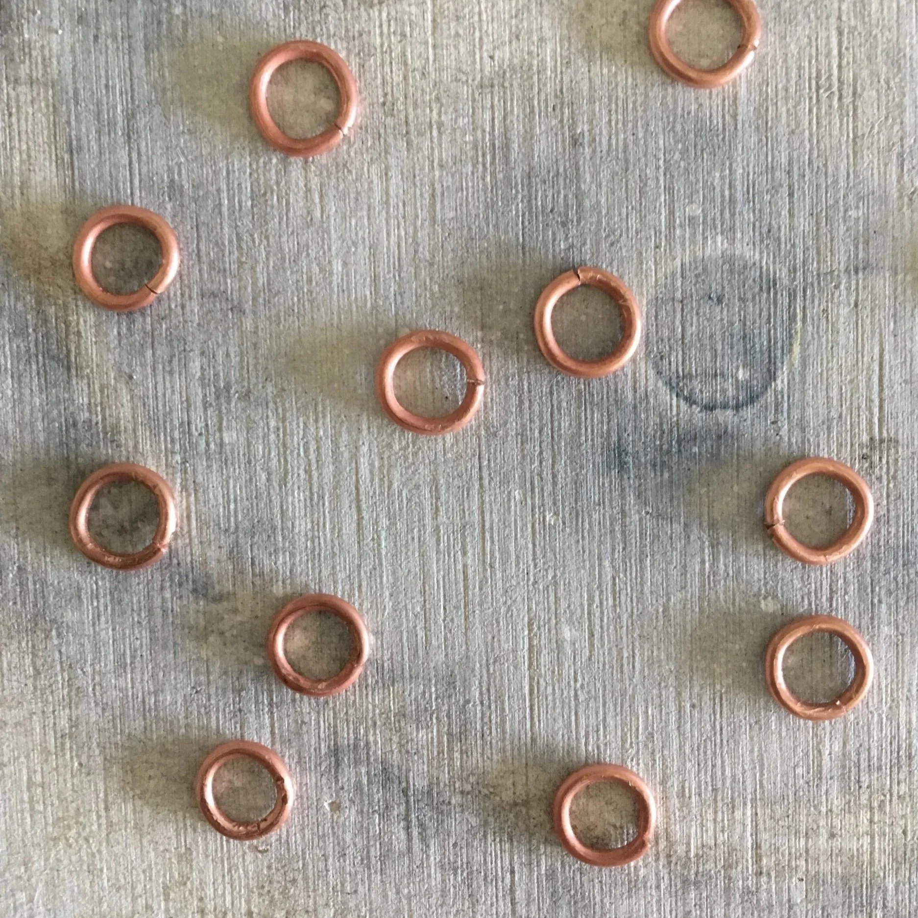 Small copper jump rings pictured on a used soldering sheet, shaped and cut, ready to be soldered into a chain