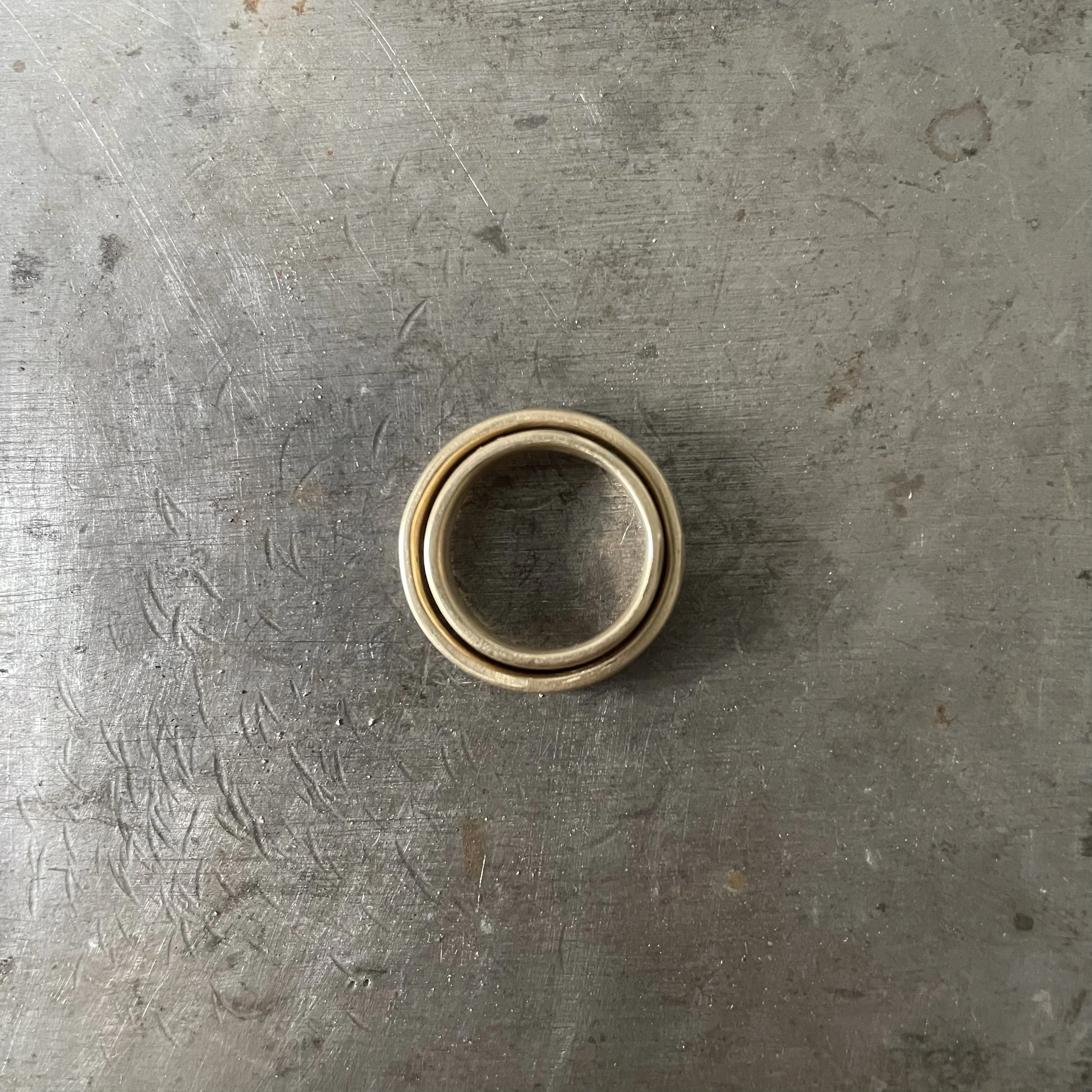 Two bespoke recycled solid gold wedding rings, one inside the other, pictured on a worn steel block