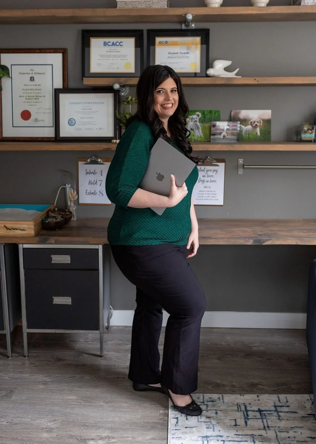 Elizabeth Nardella, RSW, RCC, smiling in her White Rock office in front of her professional credentials. Clinical consultant for social workers and counsellors in BC.