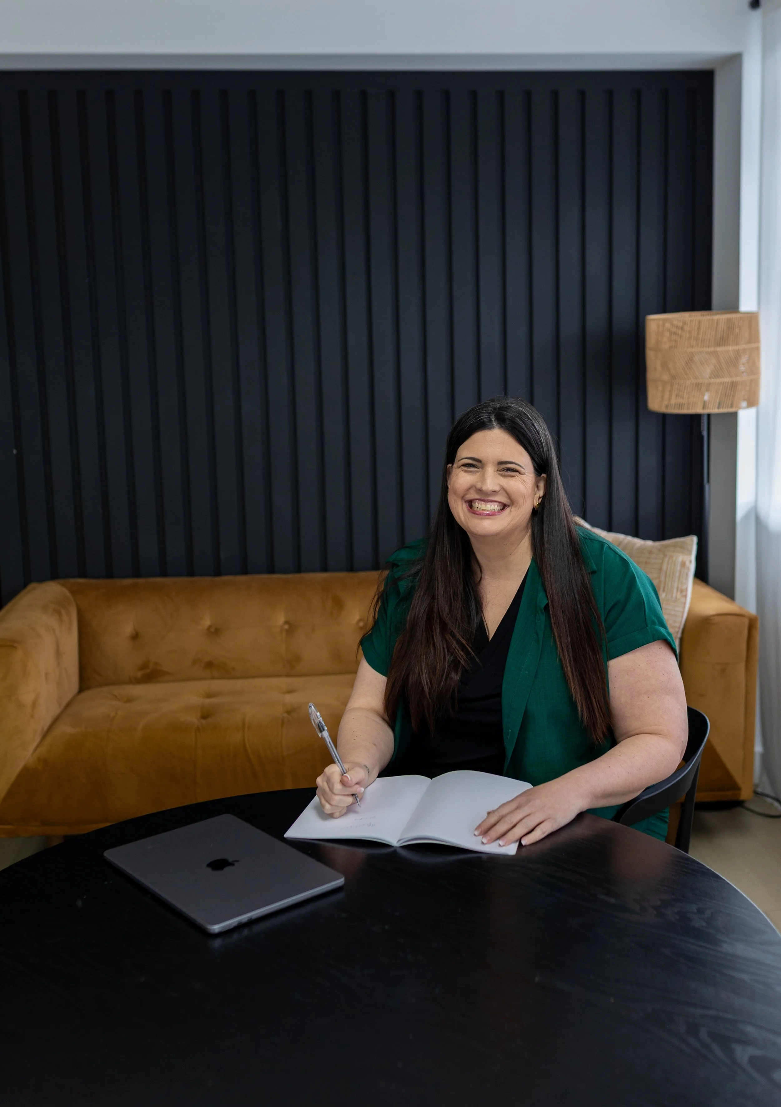 Elizabeth Nardella, RSW, RCC, clinical mentor for BC child and youth therapists, writing notes on a mustard couch