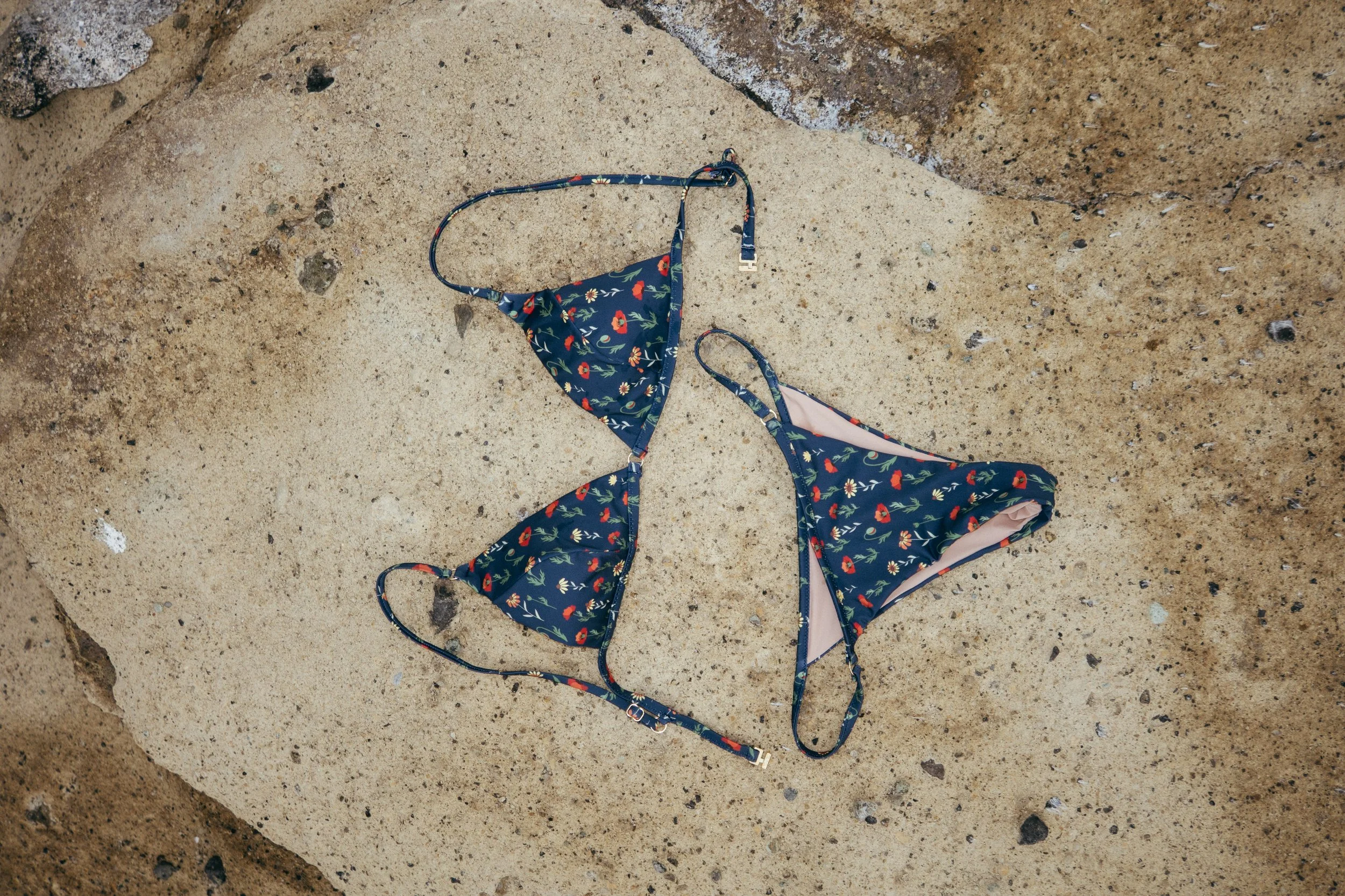Costume da bagno a due pezzi con stampa floreale, abbandonato sulla sabbia di una spiaggia.