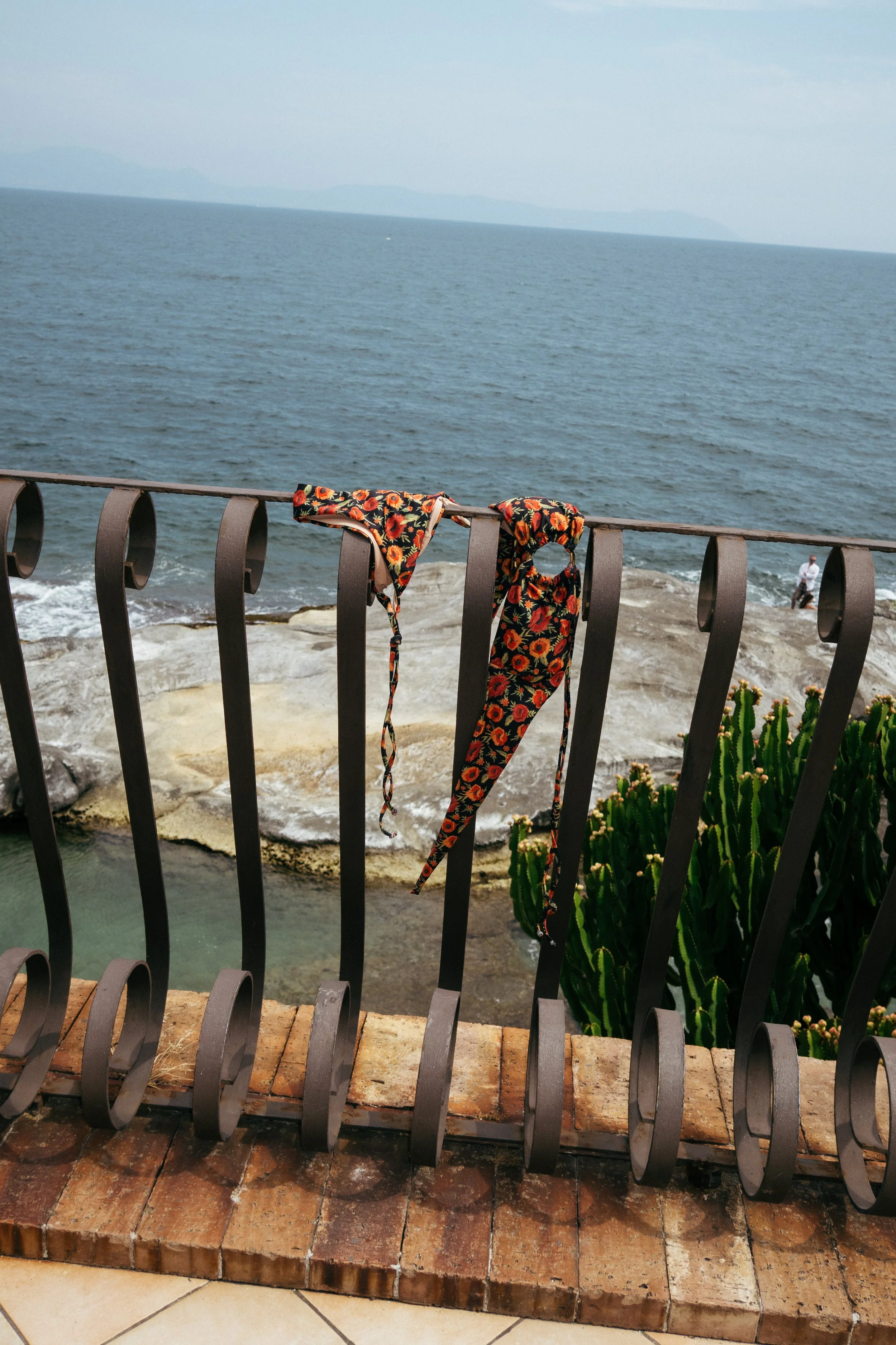 Vestito e sciarpa con disegni floreali appoggiati sulla ringhiera di un balcone che guarda il mare.
