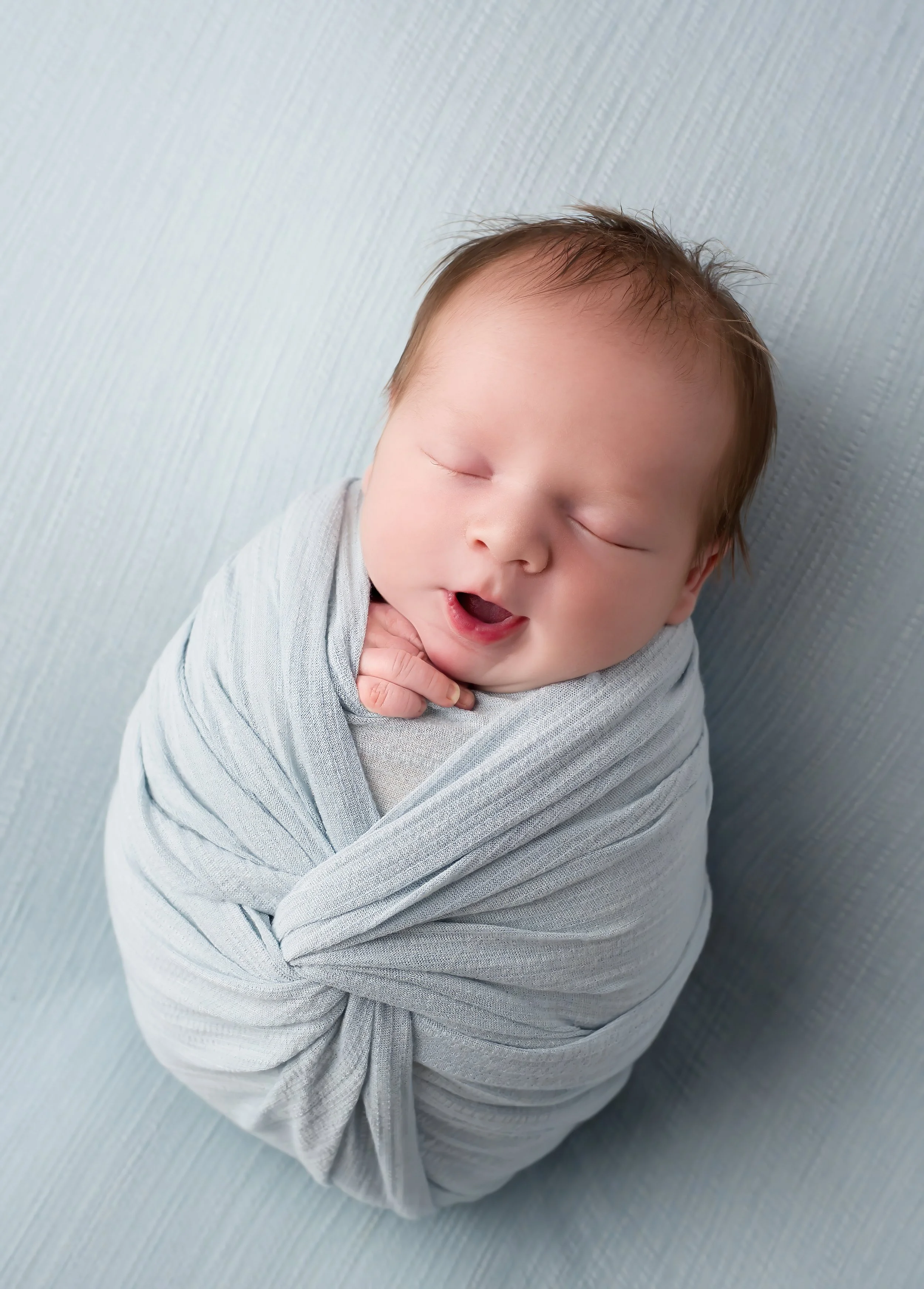 A sleeping baby wrapped in a light gray blanket, lying on a textured gray surface.