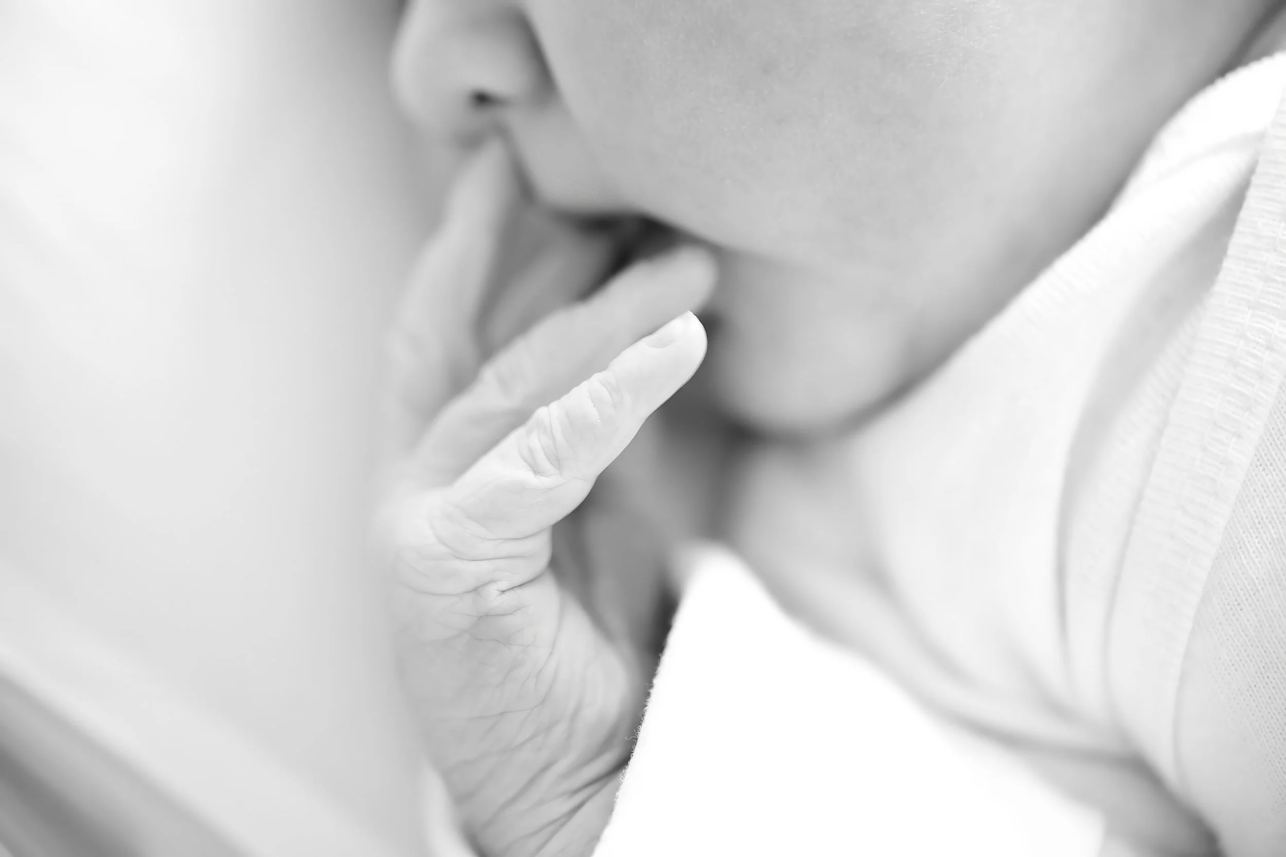 Close-up black and white photo of a newborn's face, with focus on the lips and hand gently touching the chin.