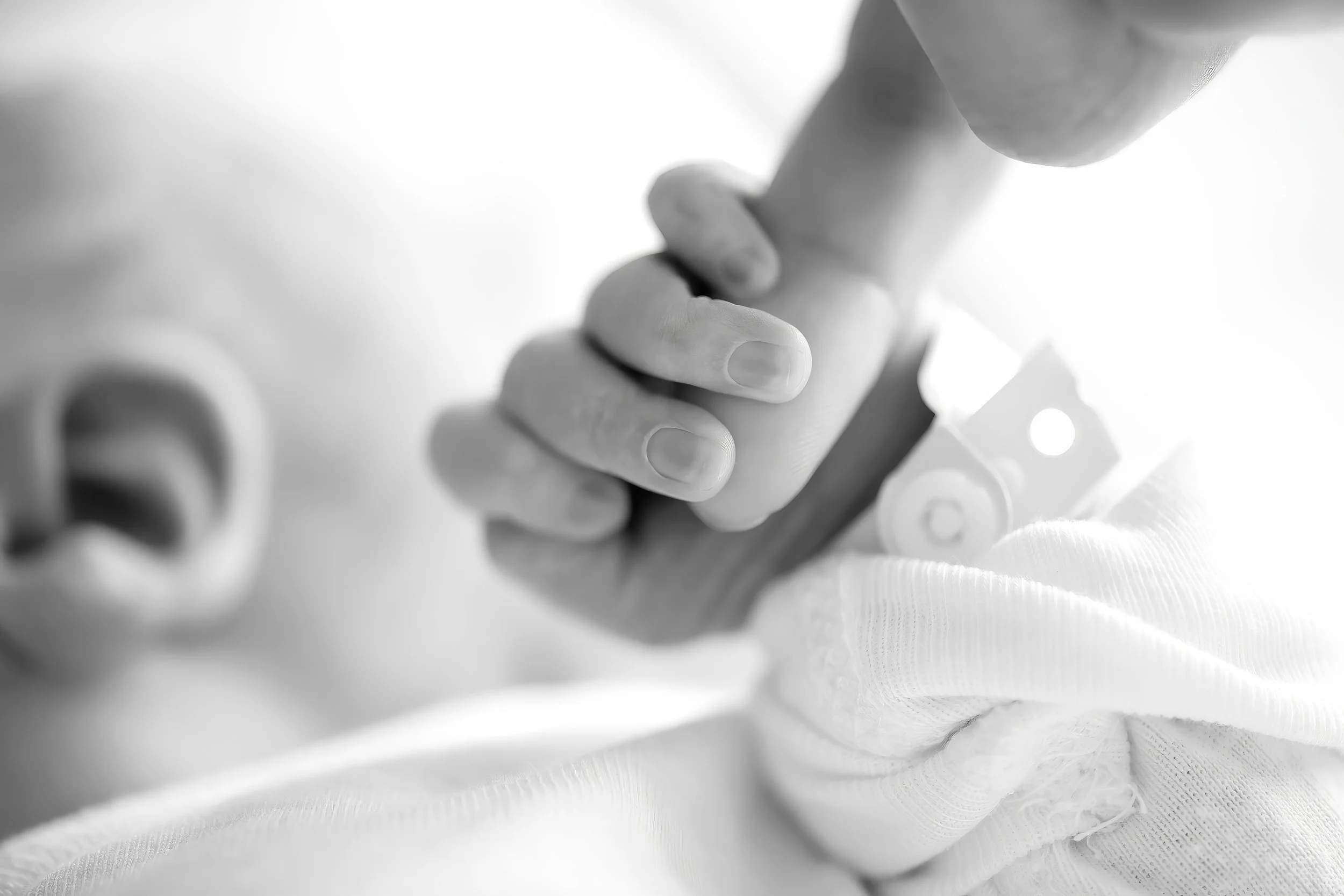 Close-up of a newborn gripping an adult's finger, with a blurred background and a white fabric surface.