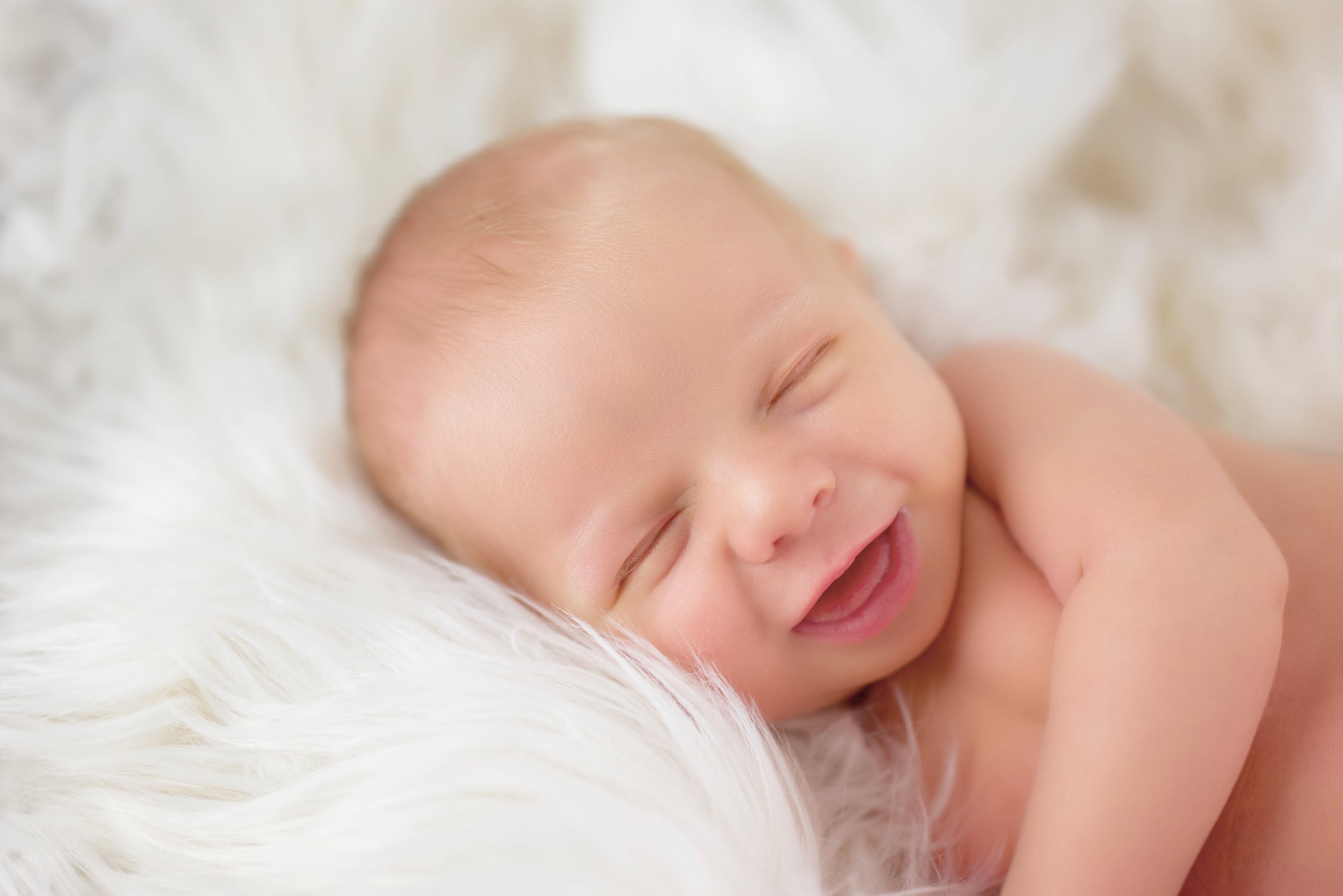 Sleeping baby smiling on a soft white blanket.