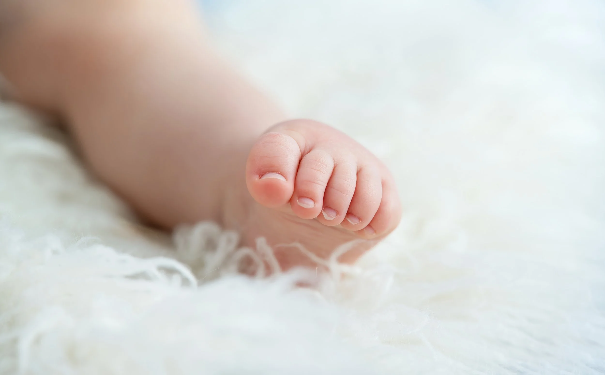 Close-up of an infant's tiny foot resting on a soft, white blanket.